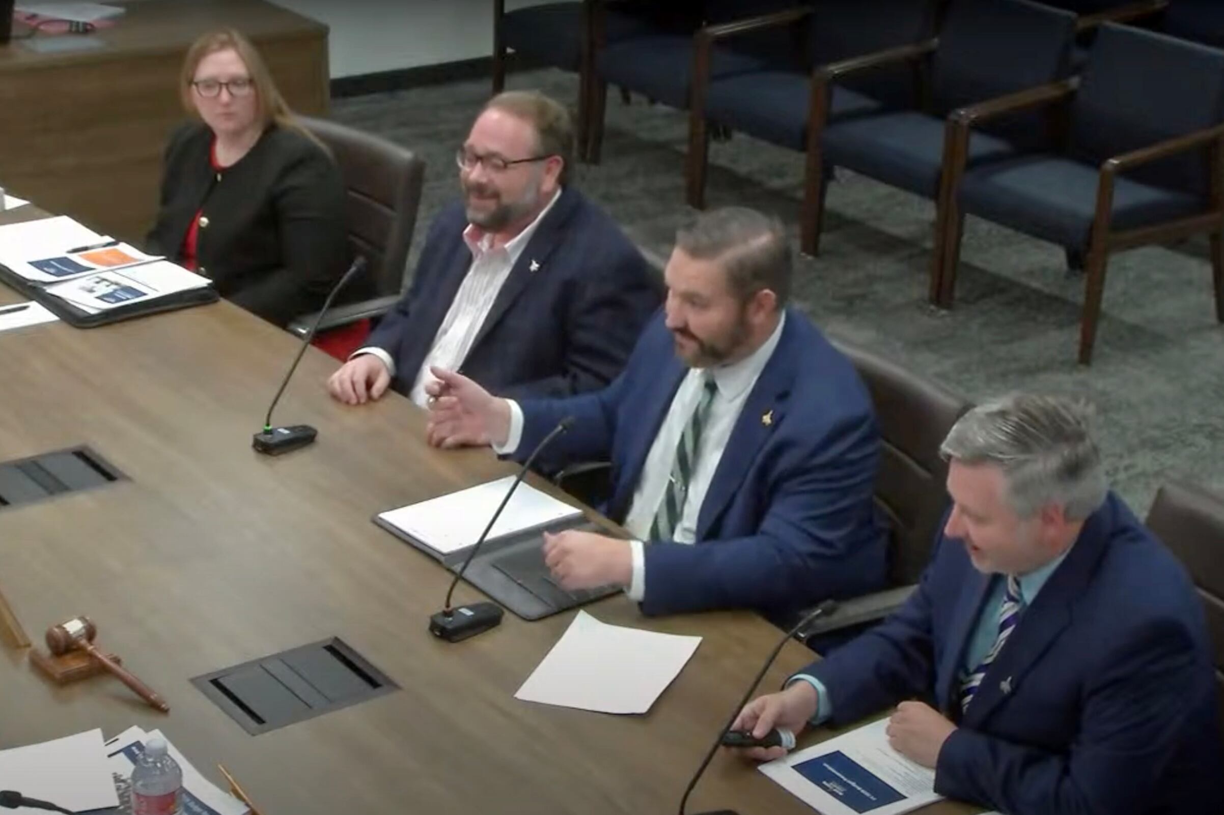 People in suits sit around a conference table.