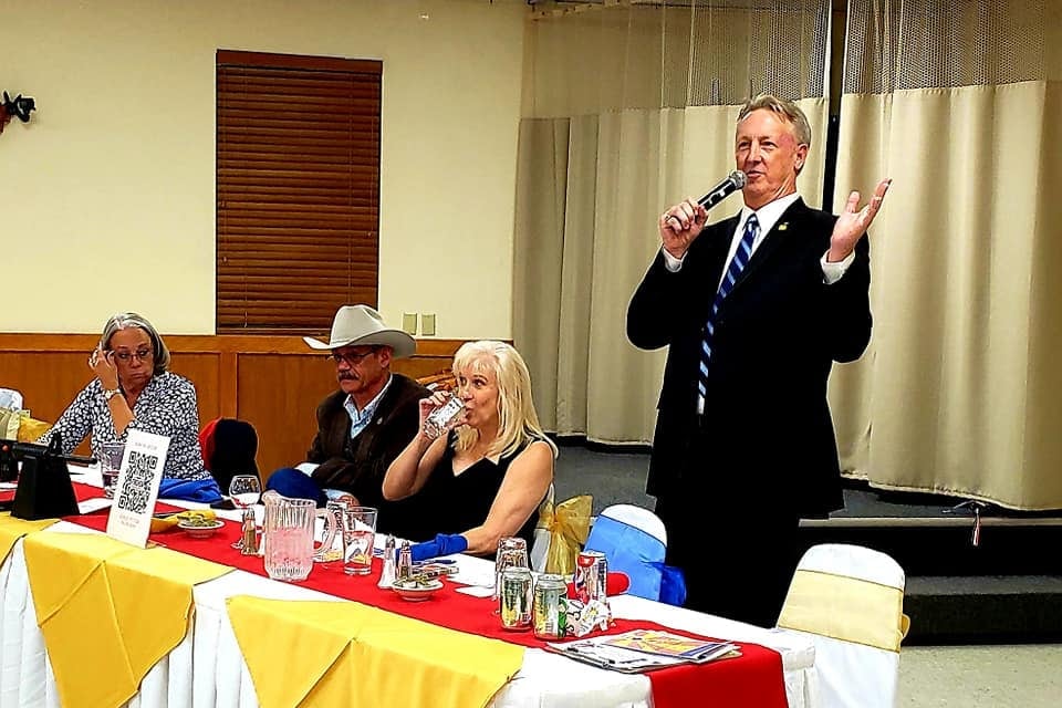 A man stands over a decorated dinner table, speaking into a microphone