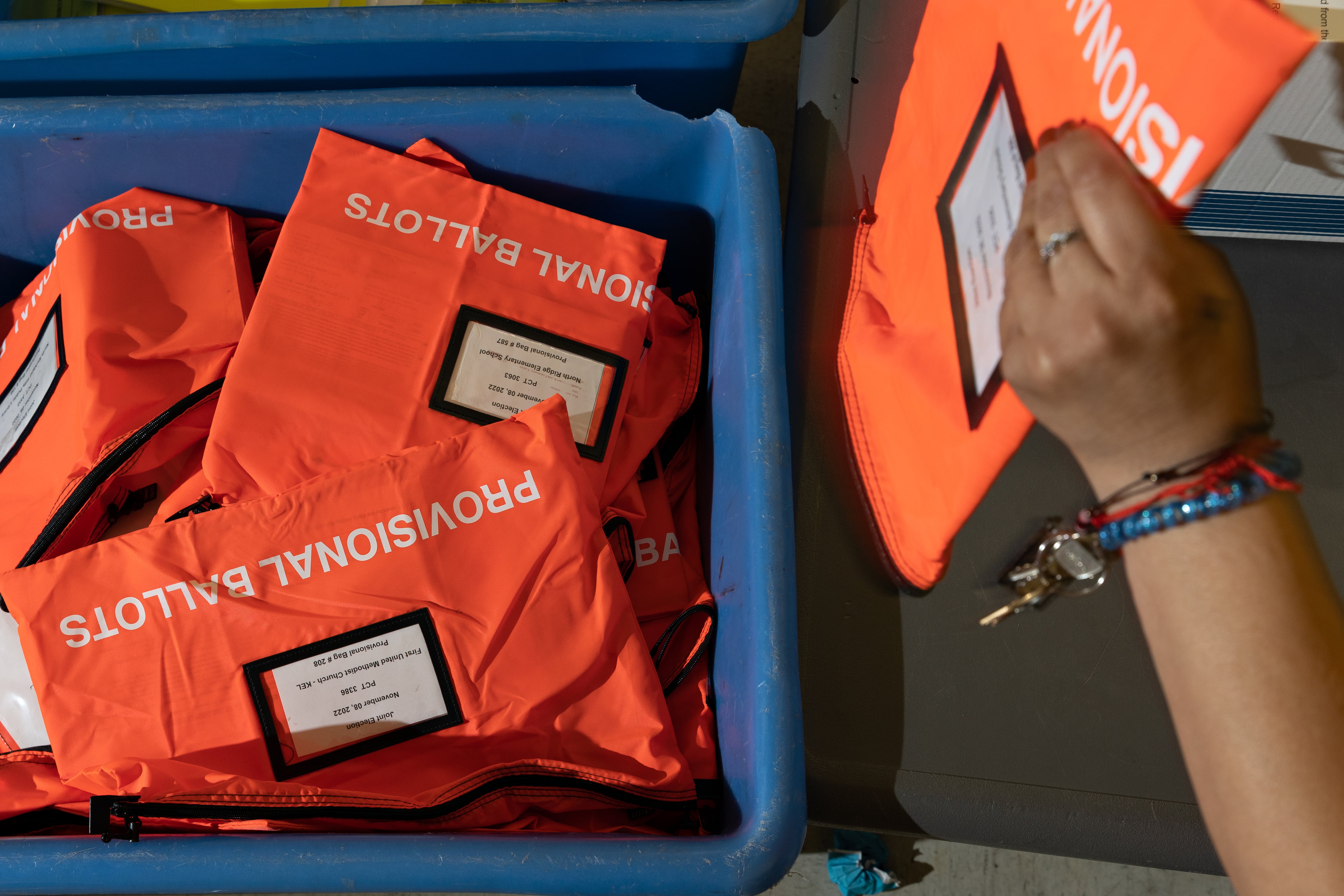 A person’s hand holding bright-colored bags labeled “provisional ballots”