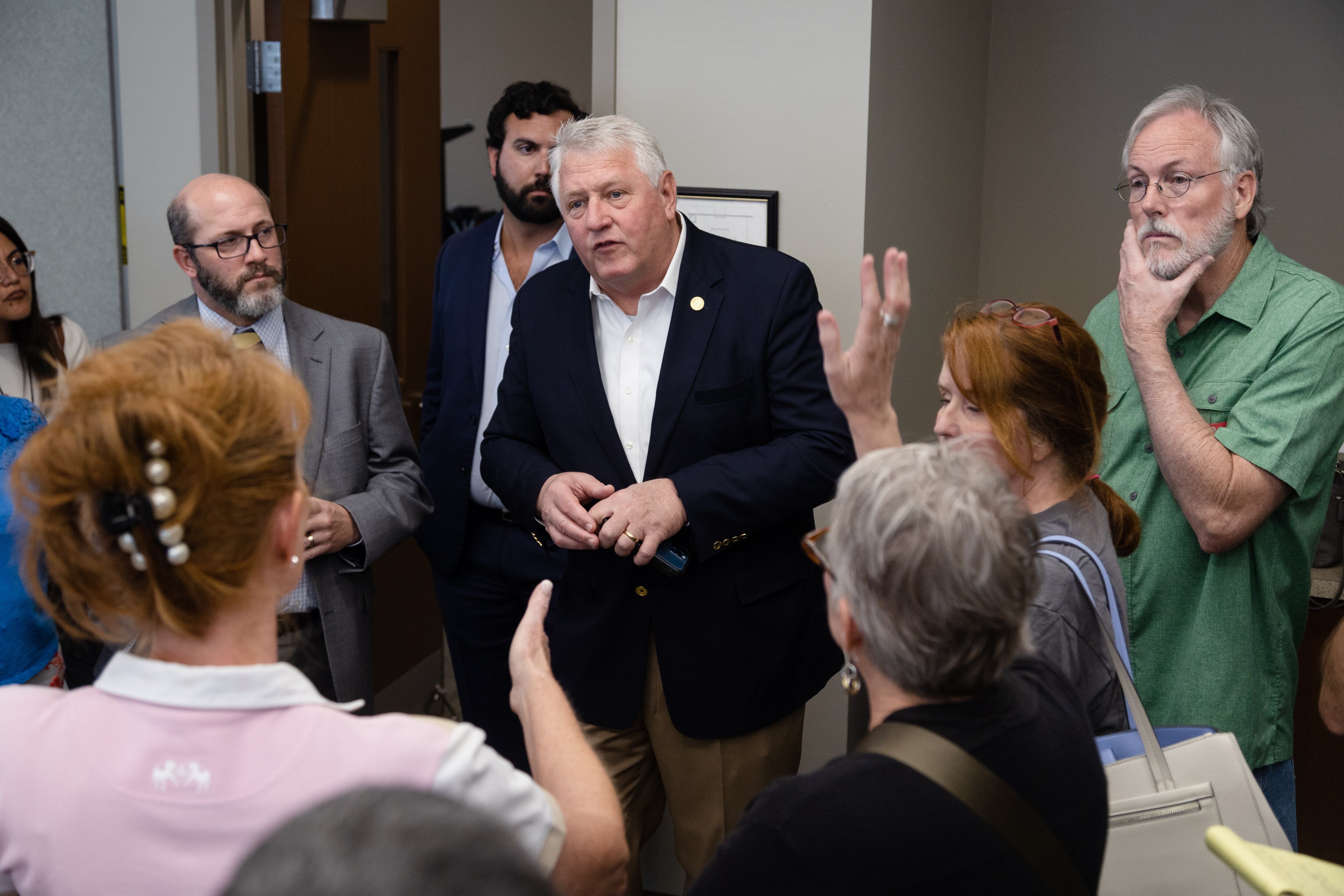 A man in a suit is surrounded by a crowd of 10 people in an office
