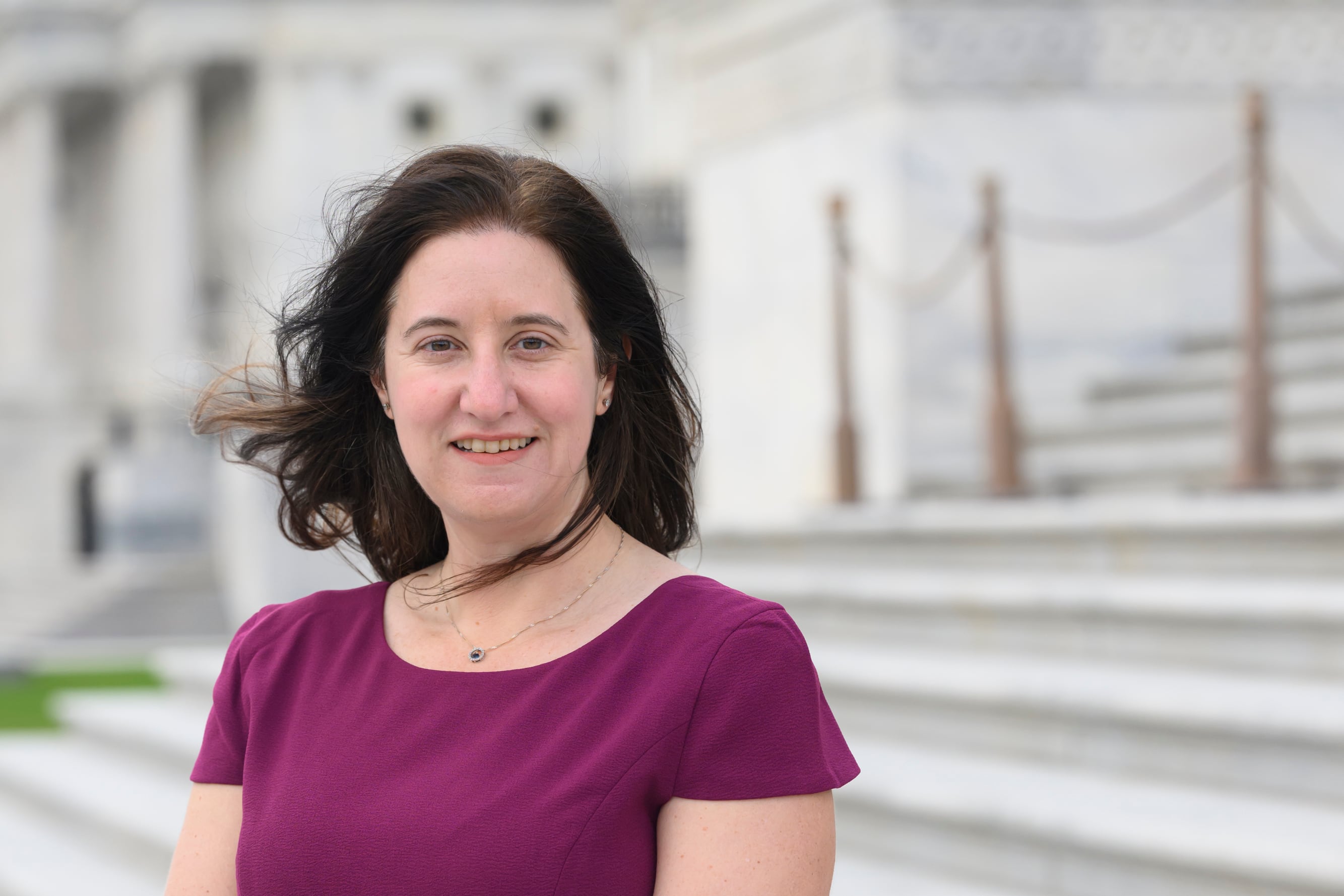 Carrie Levine, editor in chief of Votebeat, wearing a red/purple dress, standing on the steps of the U.S. Capitol in Washington D.C.
