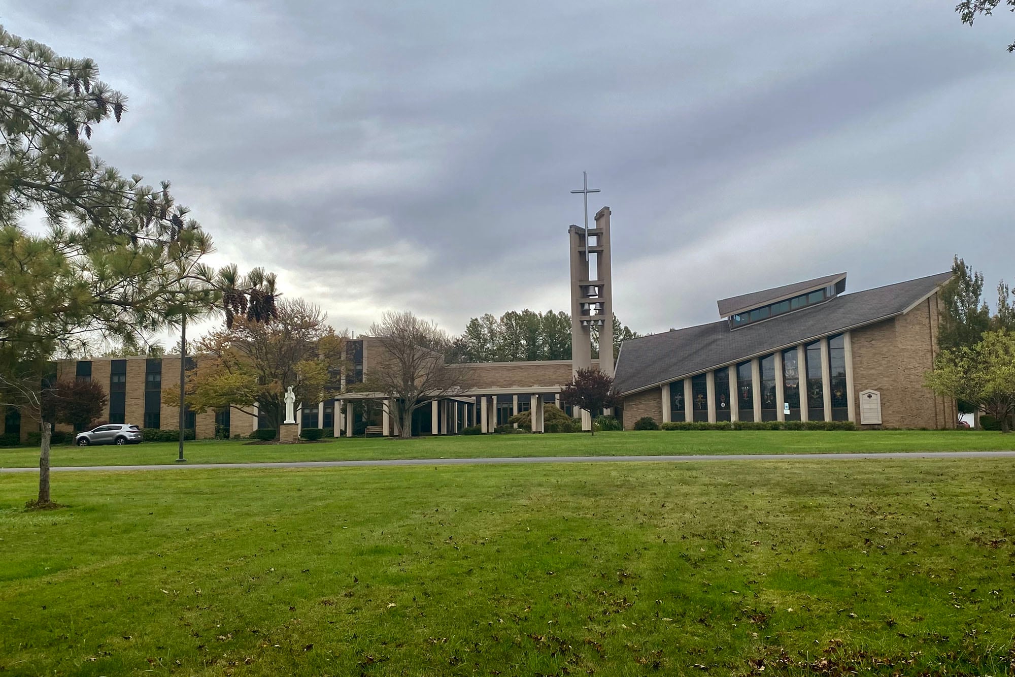 A photograph of a large building with a cross at the top and a grey sky in the background and a large greenway in the foreground.