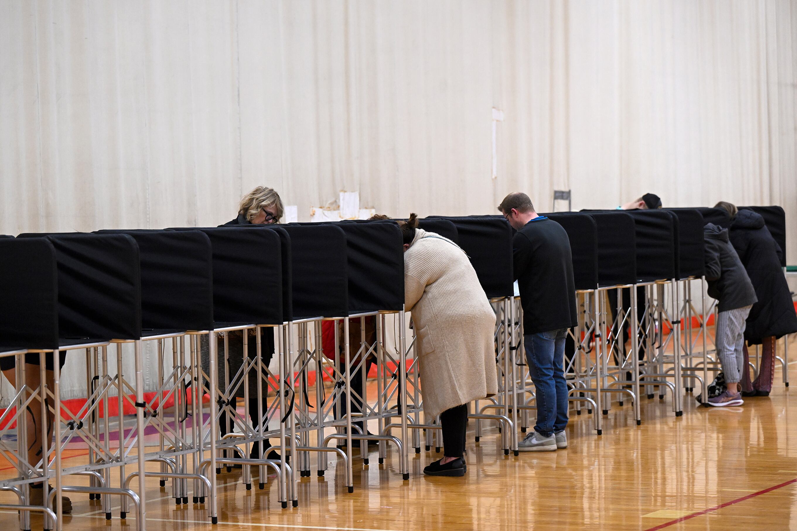 A small group of people stand at privacy tents filling out ballots in a school gym.