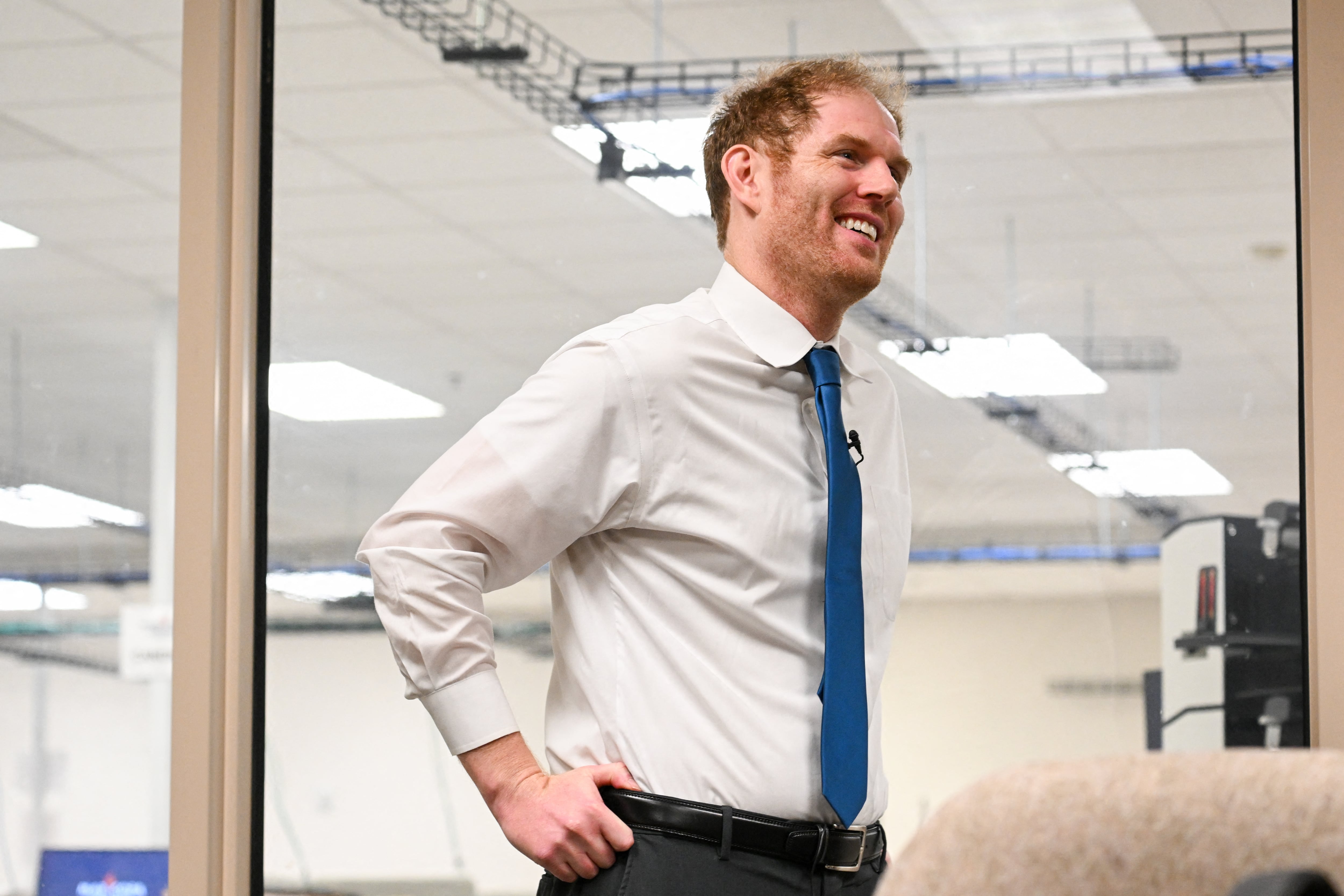 A red-headed man in white shirt and blue tie smiles while looking away