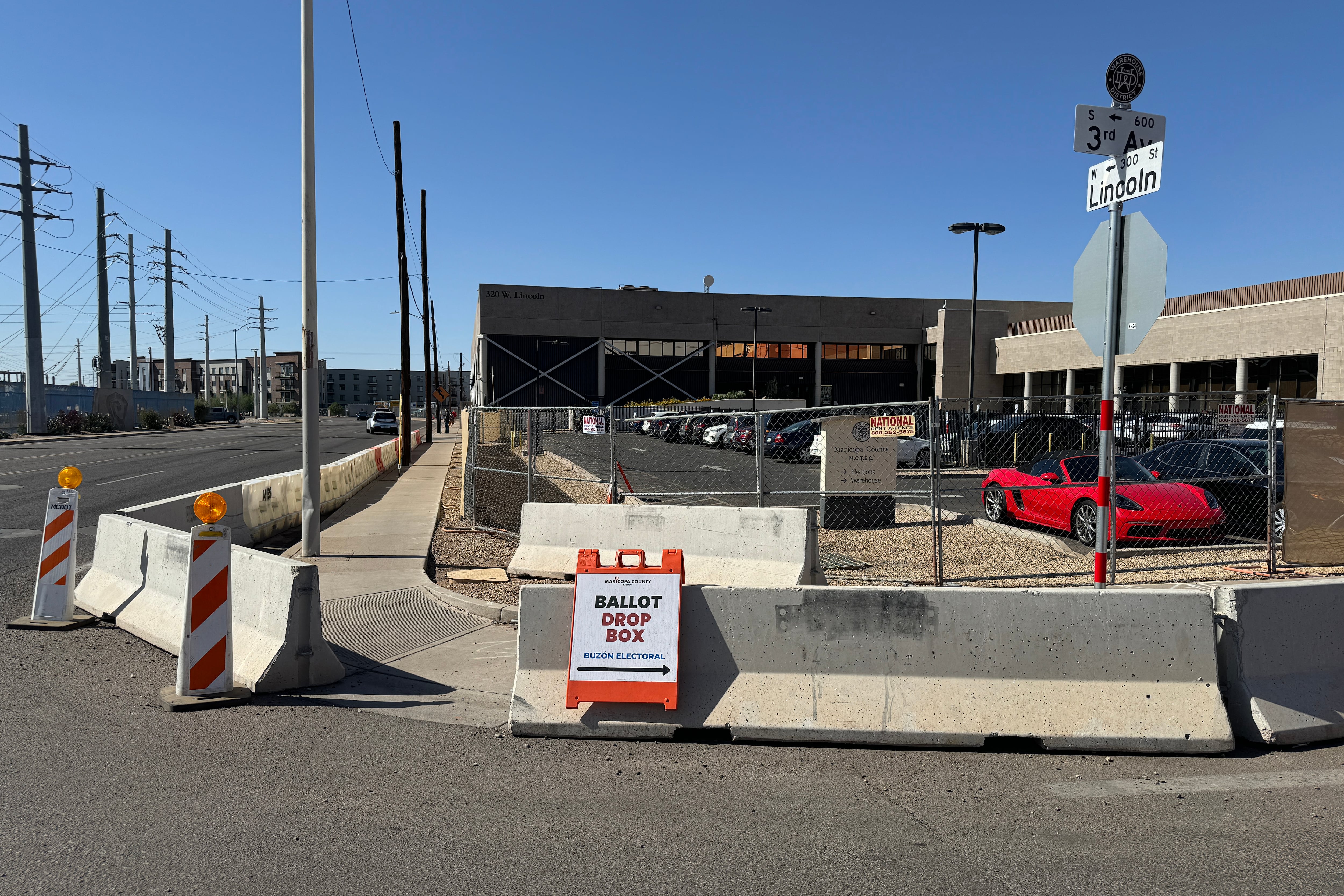 A sign leans against a giant concrete barrier in front of a building with blue sky in the background.
