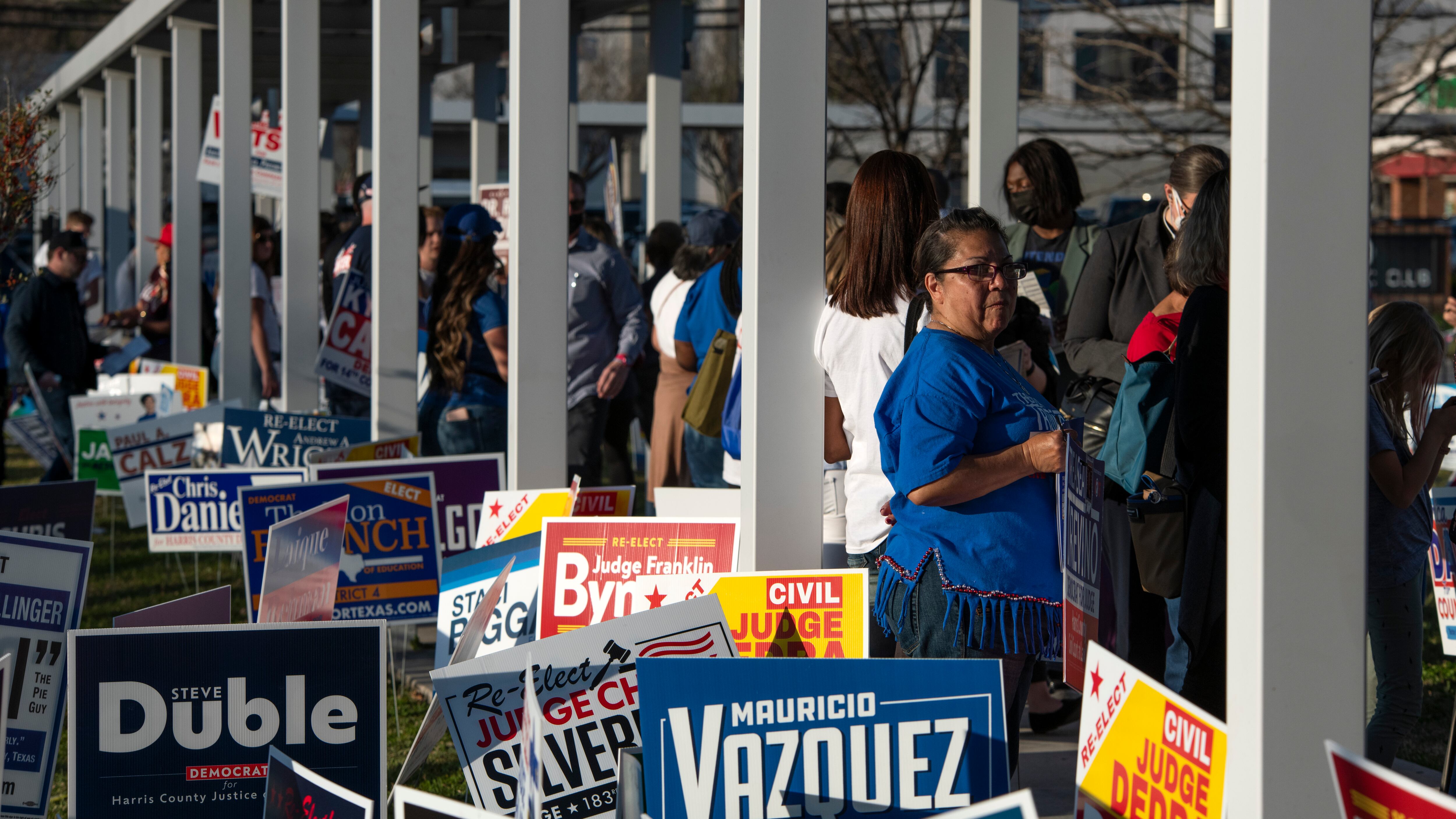 A woman looks over her shoulder in a long line surrounded by campaign signs