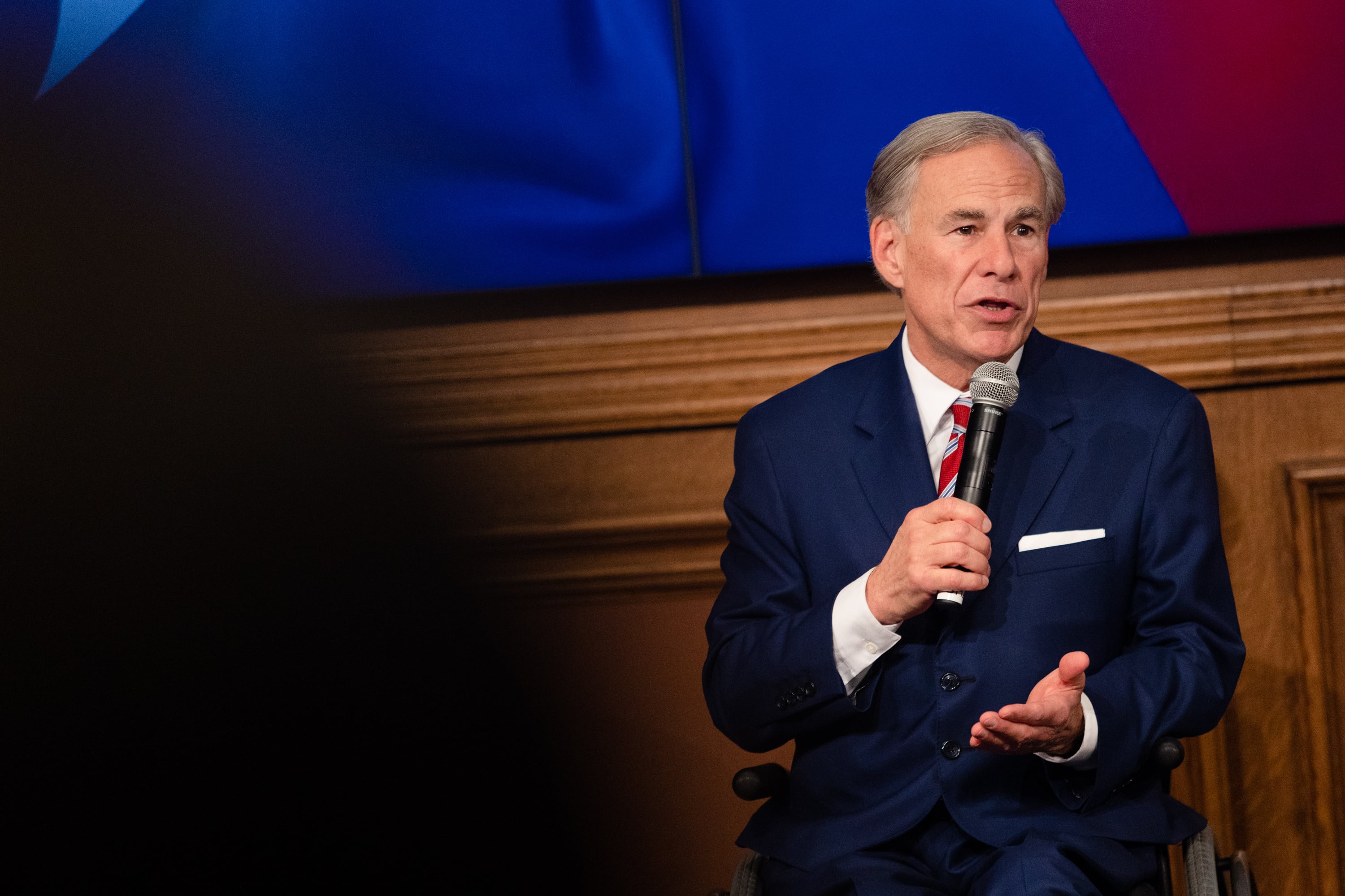 A man in a suit speaks while holding a microphone