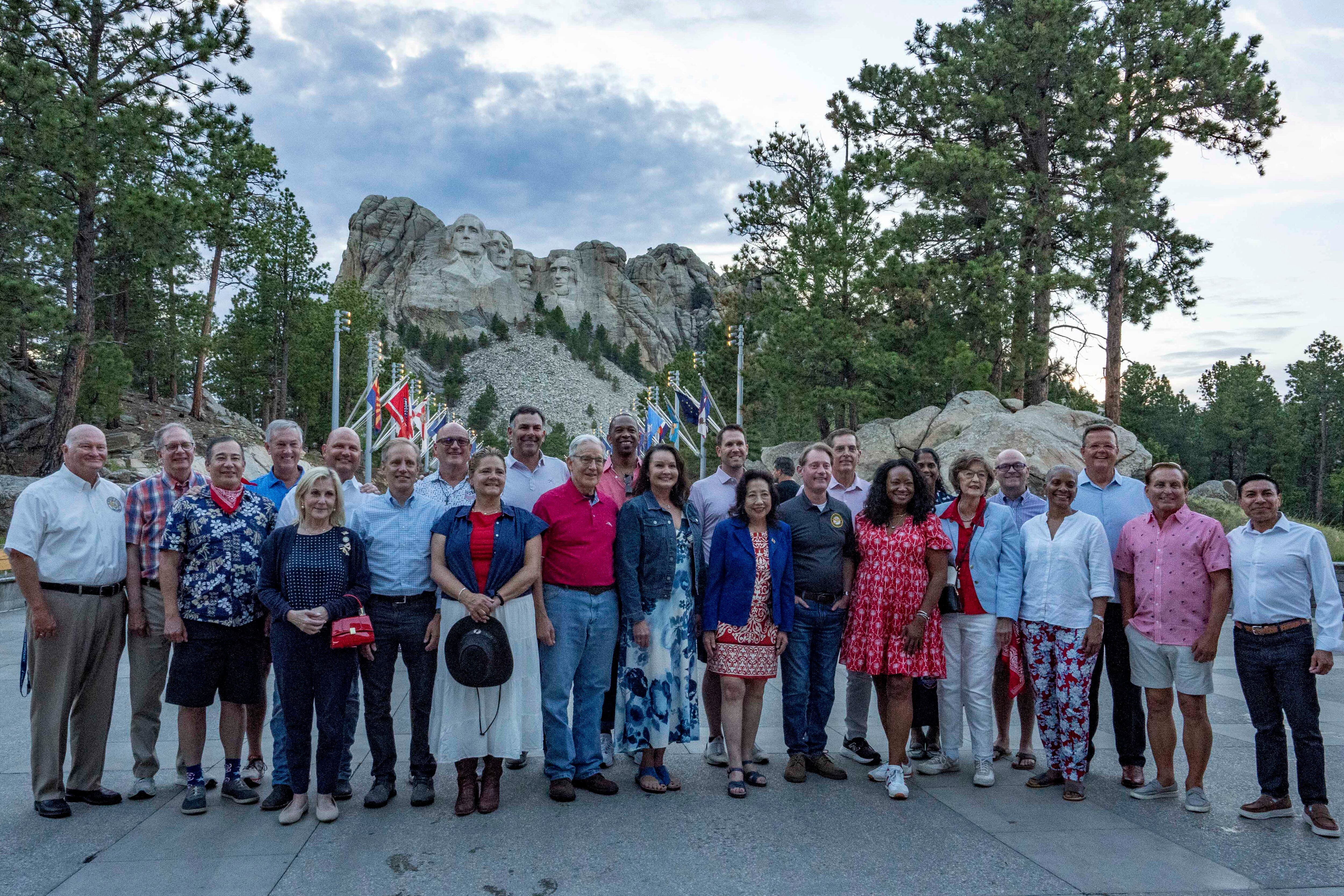 A large group of people pose for a photograph with Mount Rushmore in the background.
