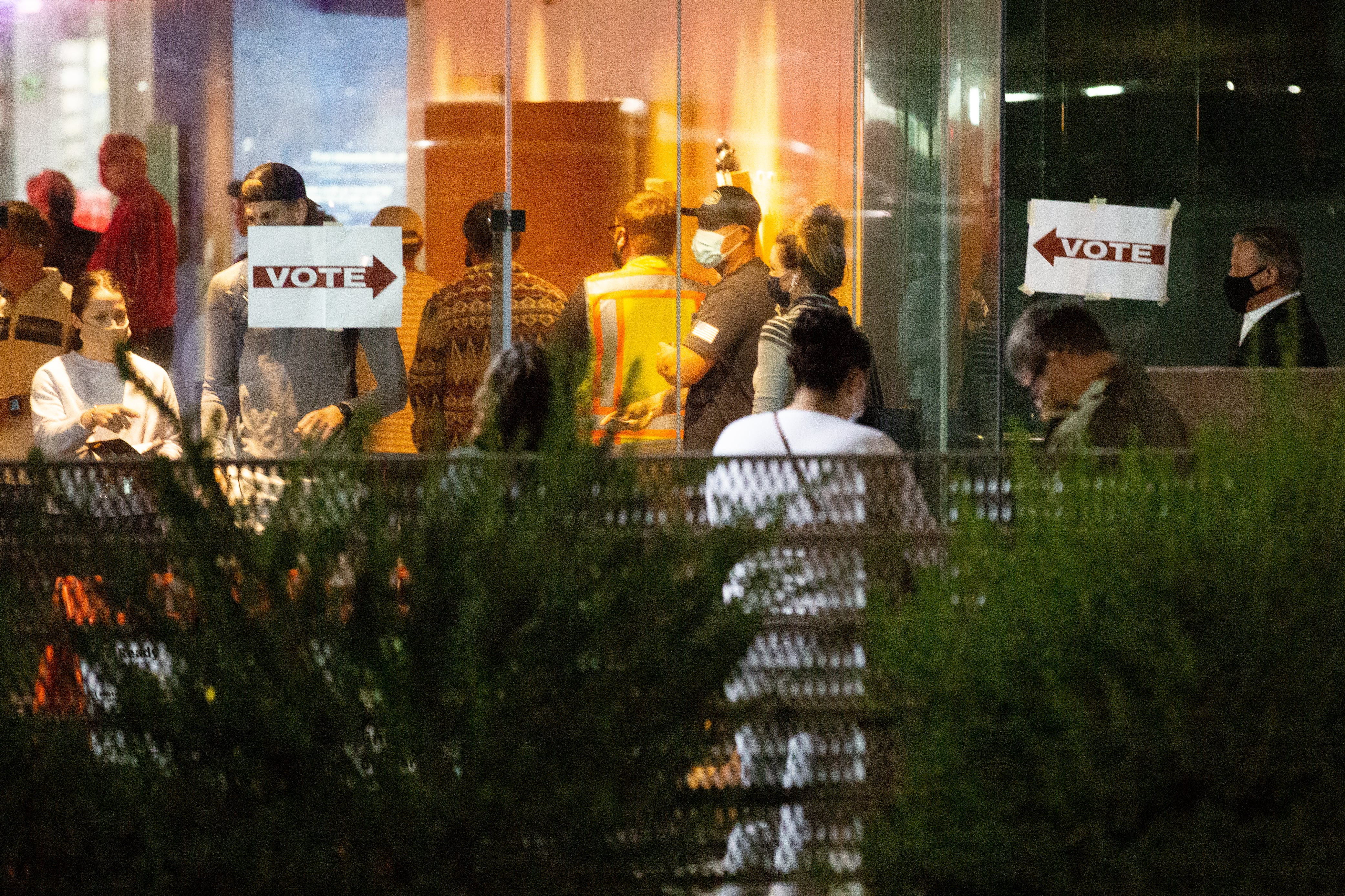 Voters line up outside of the glass doors of a polling site, with white signs and red writing directing them to the entrance.