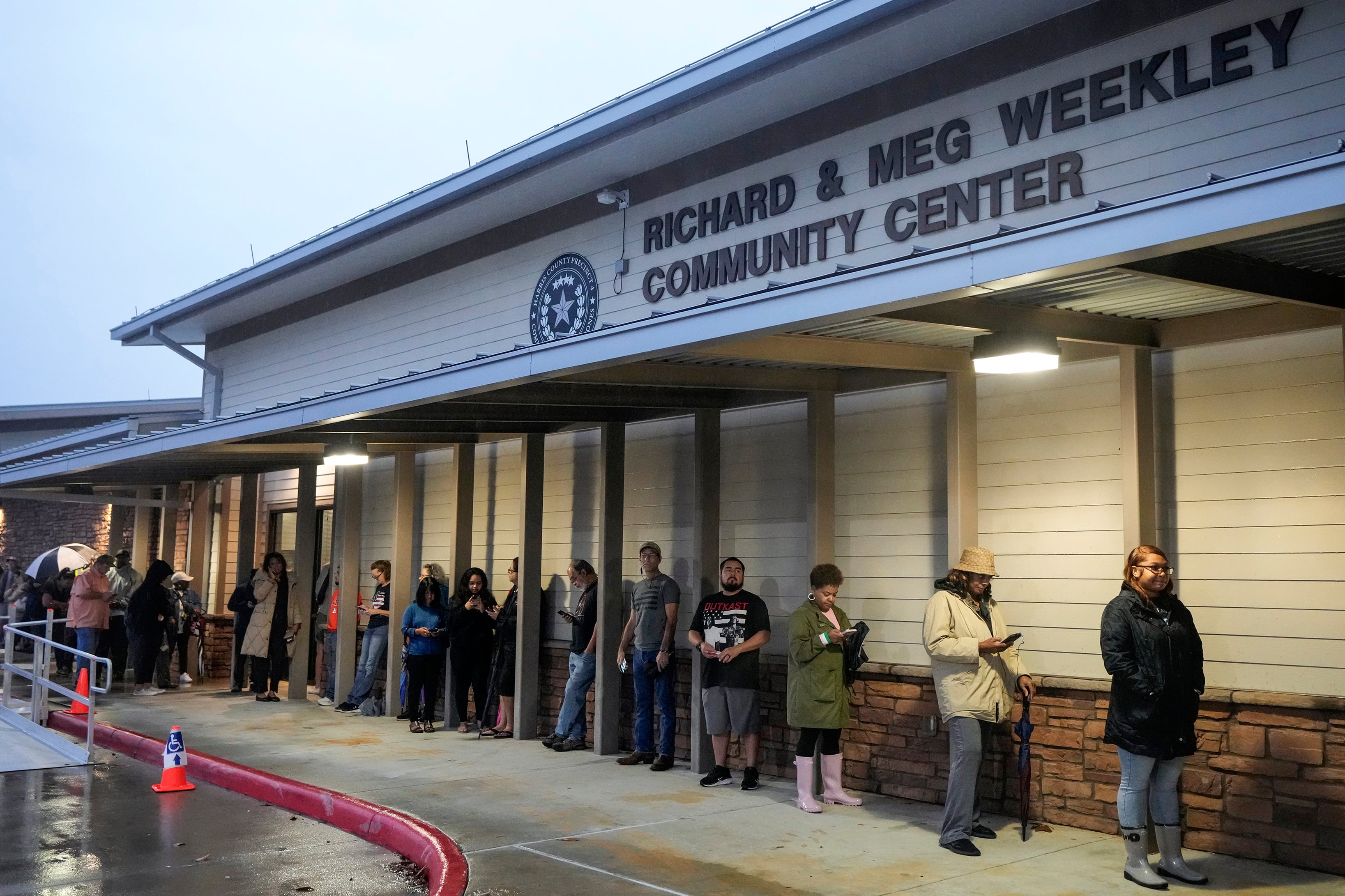 A line of people stand outside of a community center building.