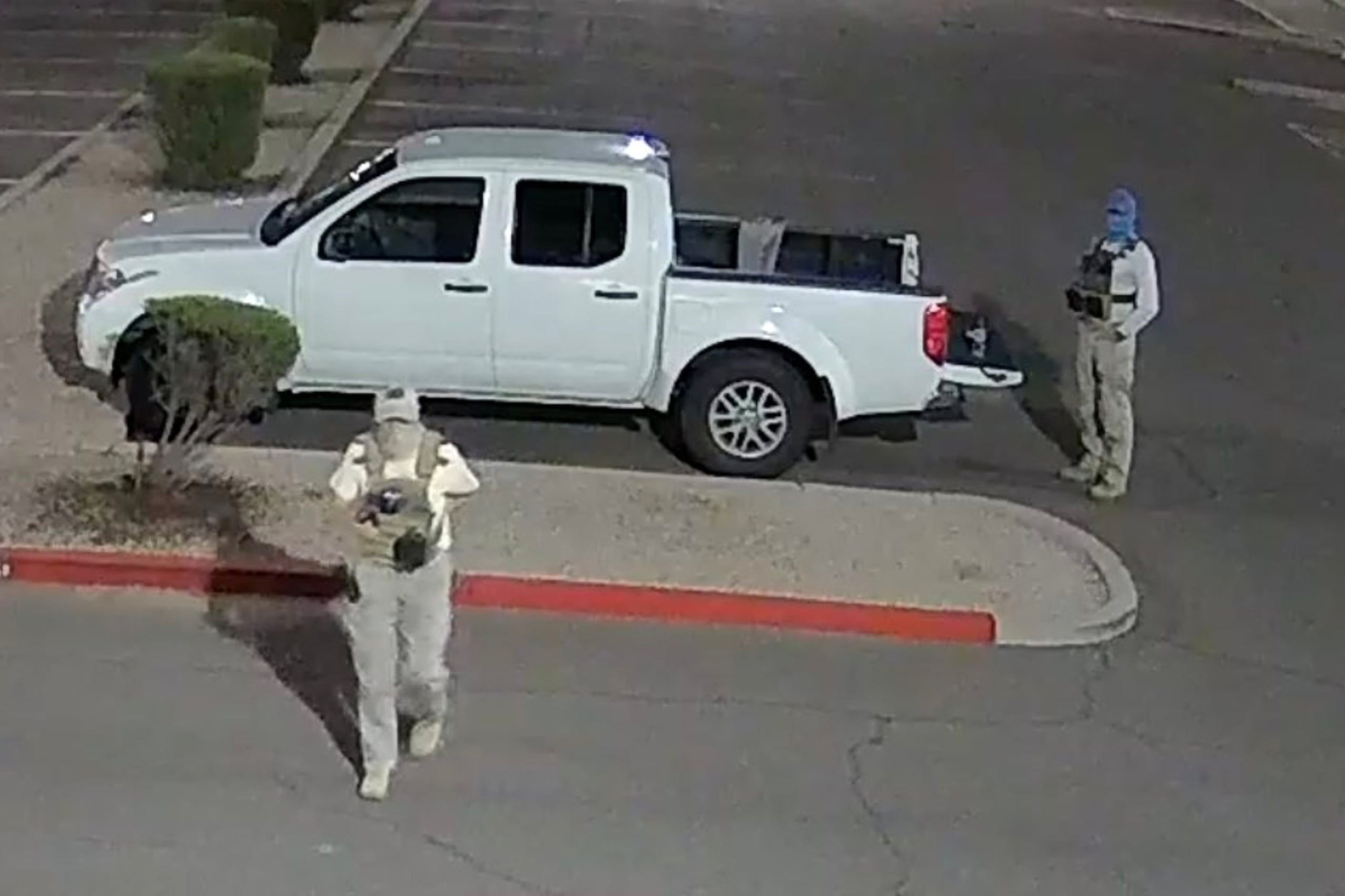 Two people with their identities shielded and holding guns stand near a white truck outside in a parking lot.
