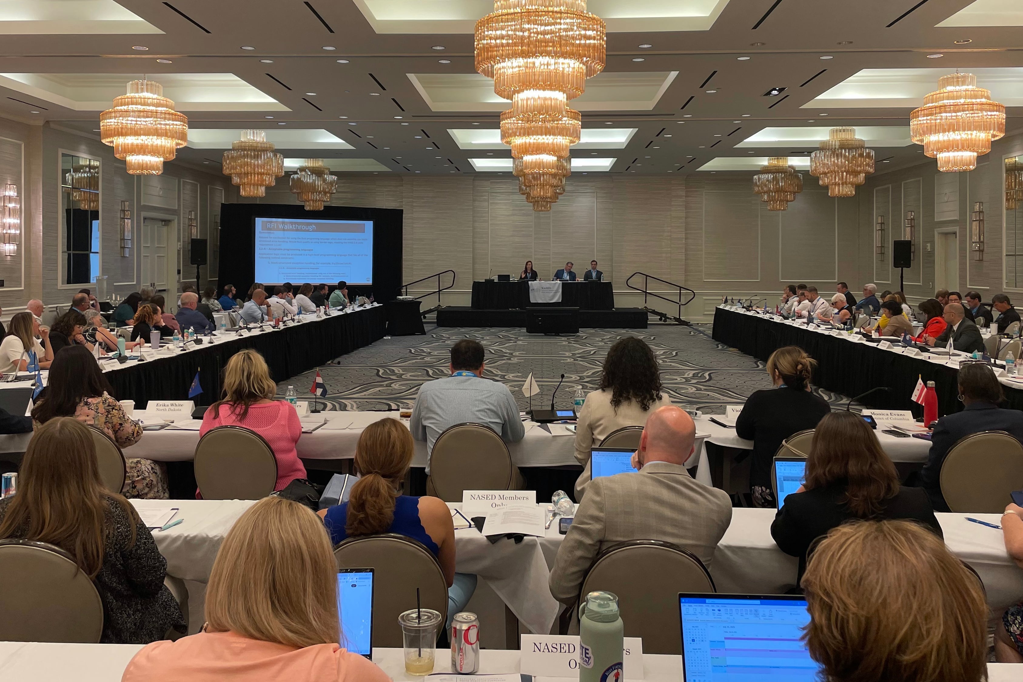A photograph of a room full of a large group of people sitting at tables around a large conference room.