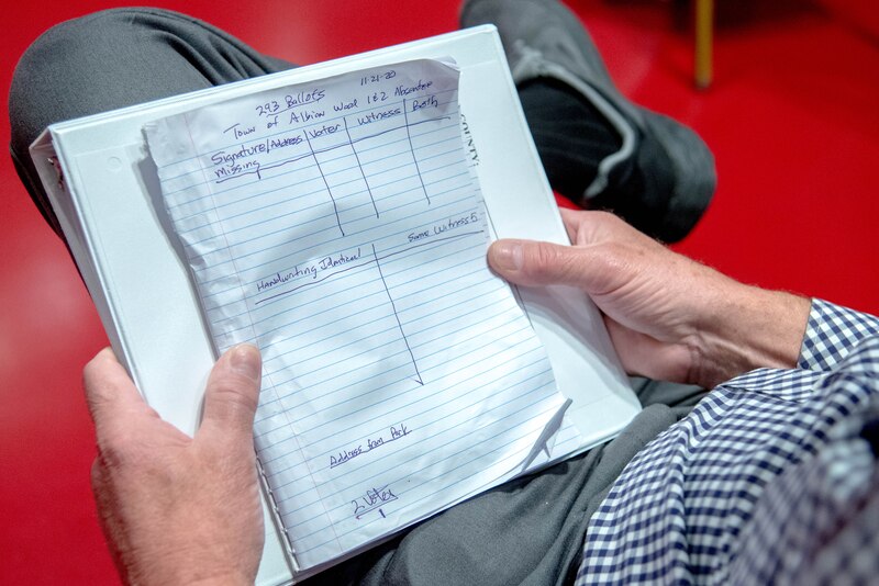 A close up of a white paper with black writing and a person holding it on their lap.