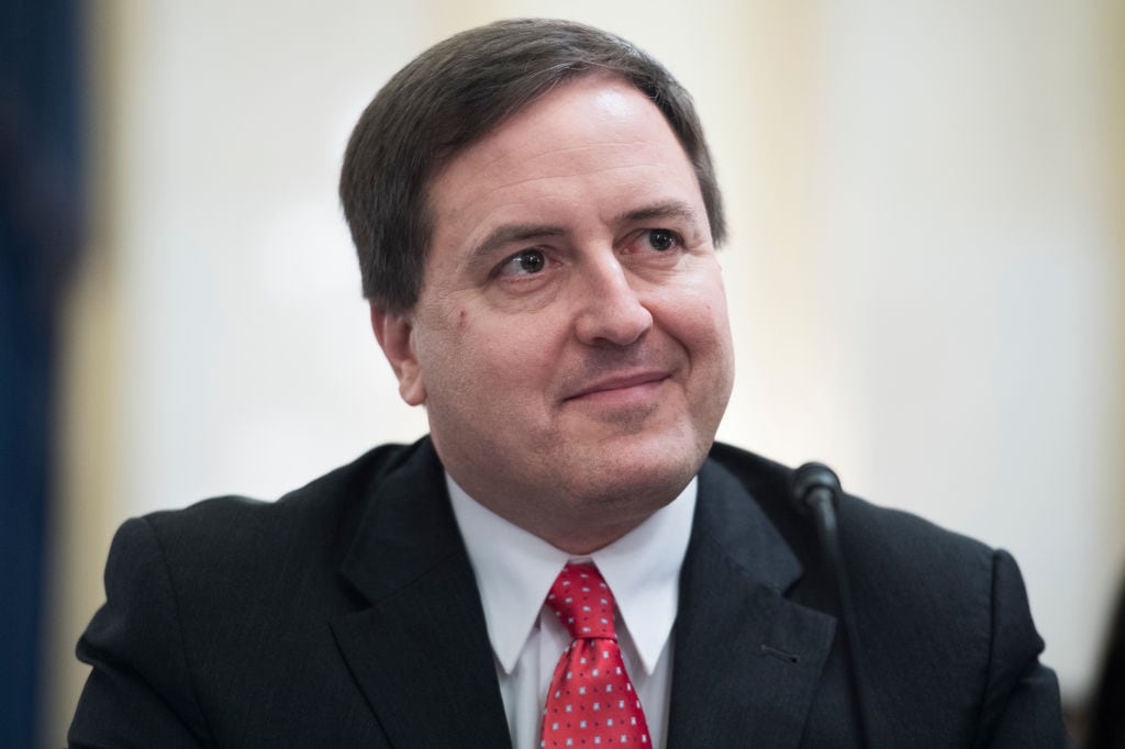 Portrait of a brown-haired man with a red tie and dark suit.