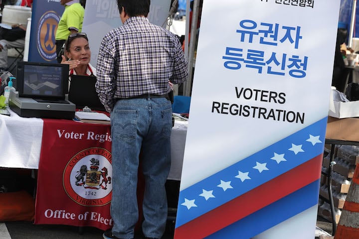 A woman seated as a table, speaking to a standing man, surrounded by signs reading “voter registration”