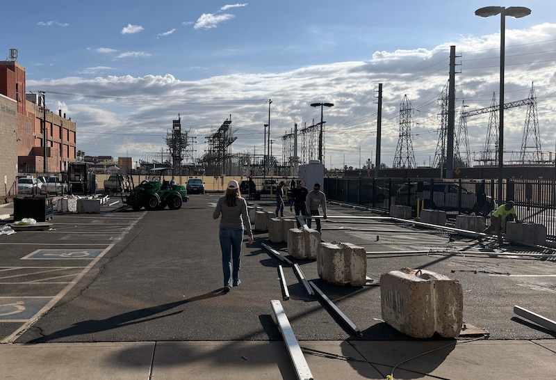 A woman walks near a crew of people constructing a fence outside.