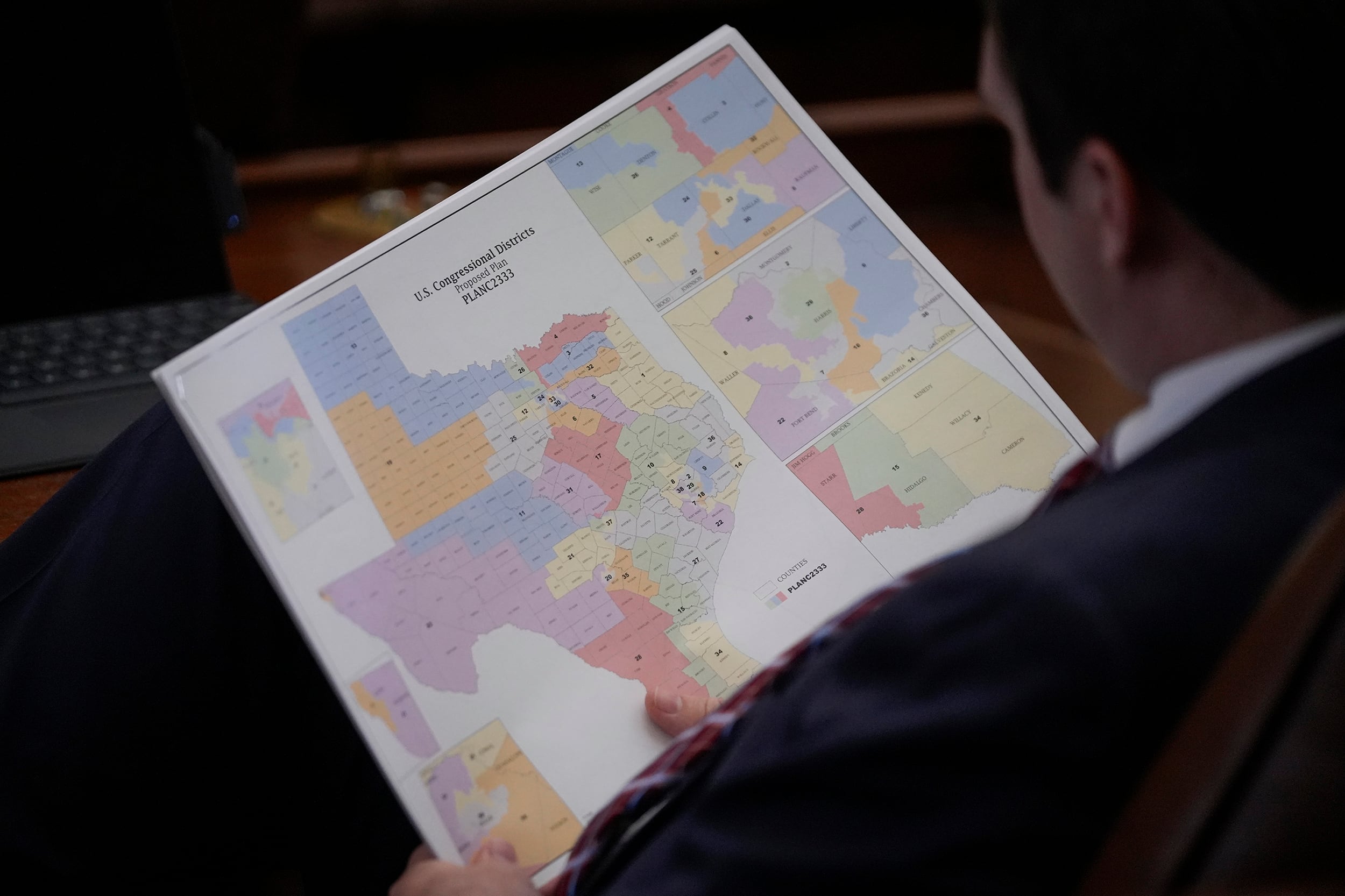 A photograph of a man holding a large piece of paper showing a colorful map of the state of texas.