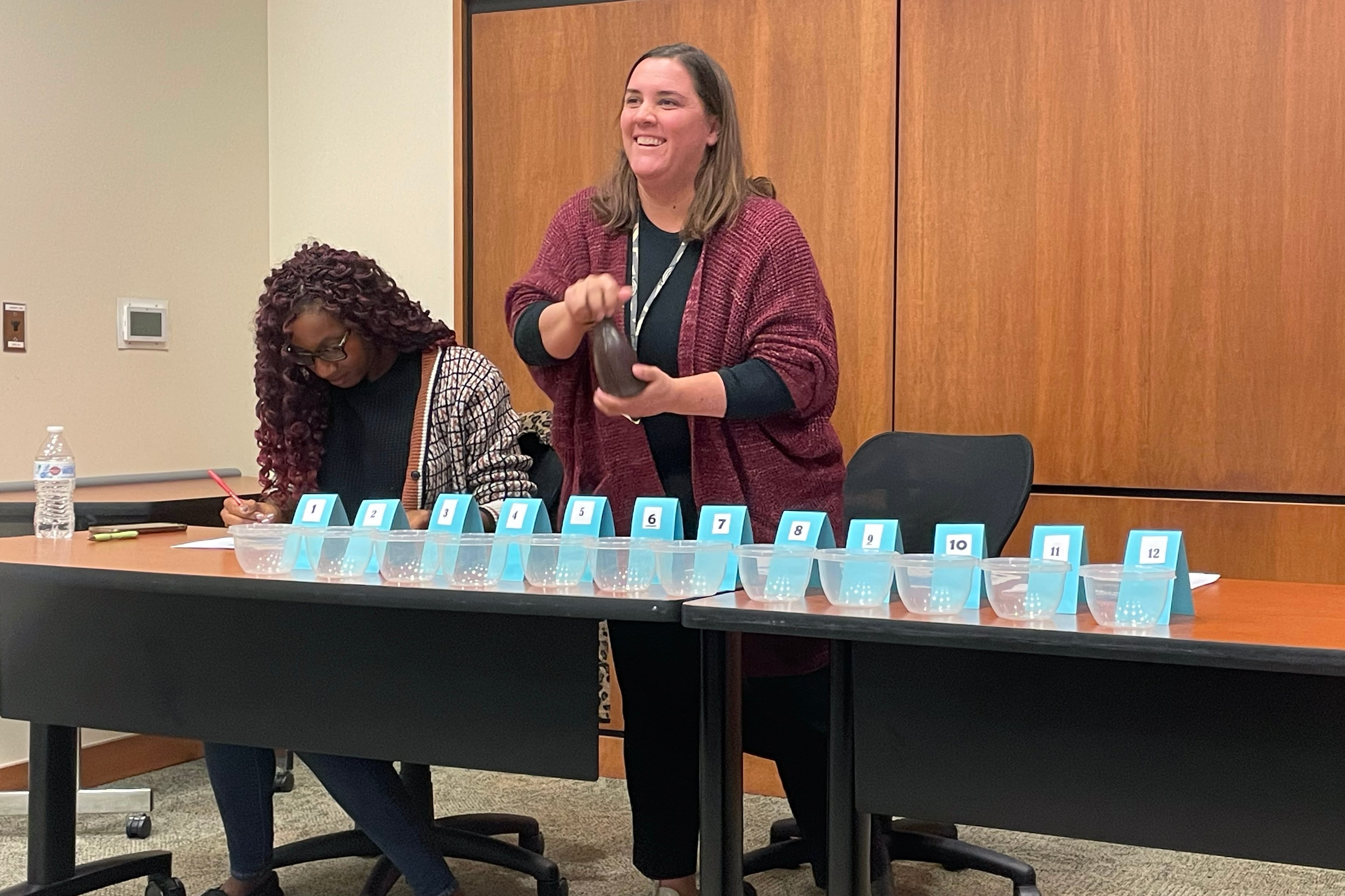 A photograph of two women working at a table in a conference room with blue numbered pieces of paper on the table.