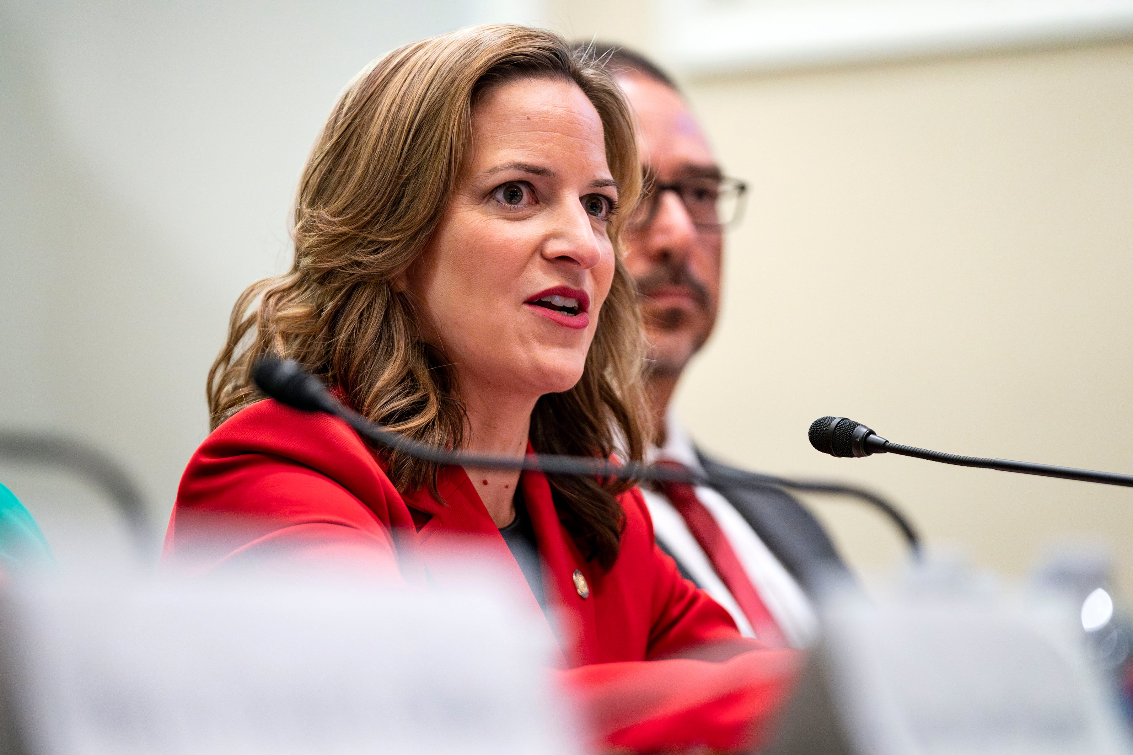 A woman in a red suit speaks into a small microphone.