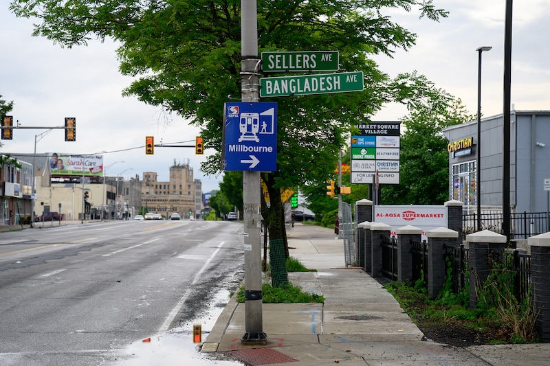 A street sign on a large pole near a sidewalk and an empty street on a cloudy day.