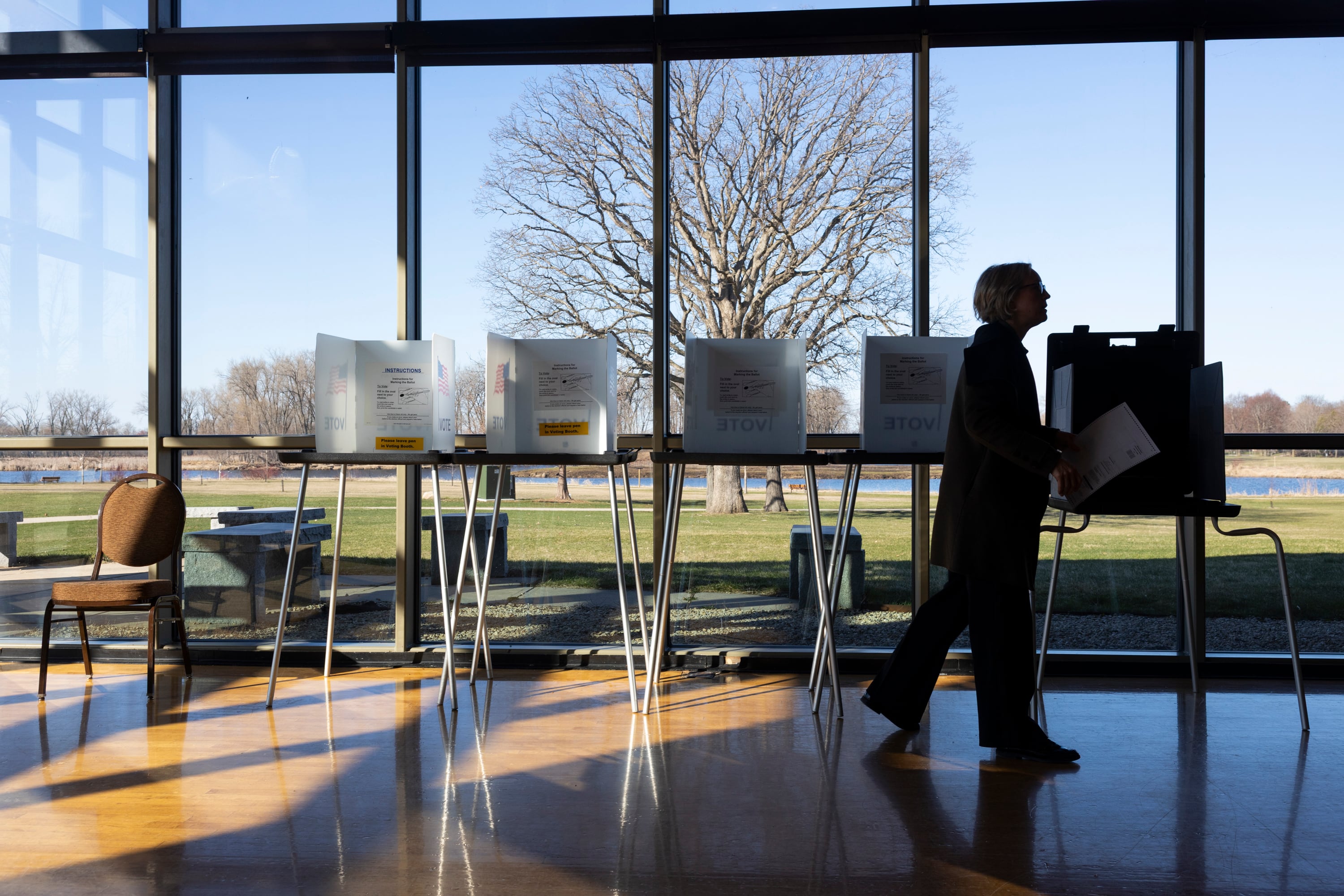 A person walking in front of the voting booths stood by a large window.