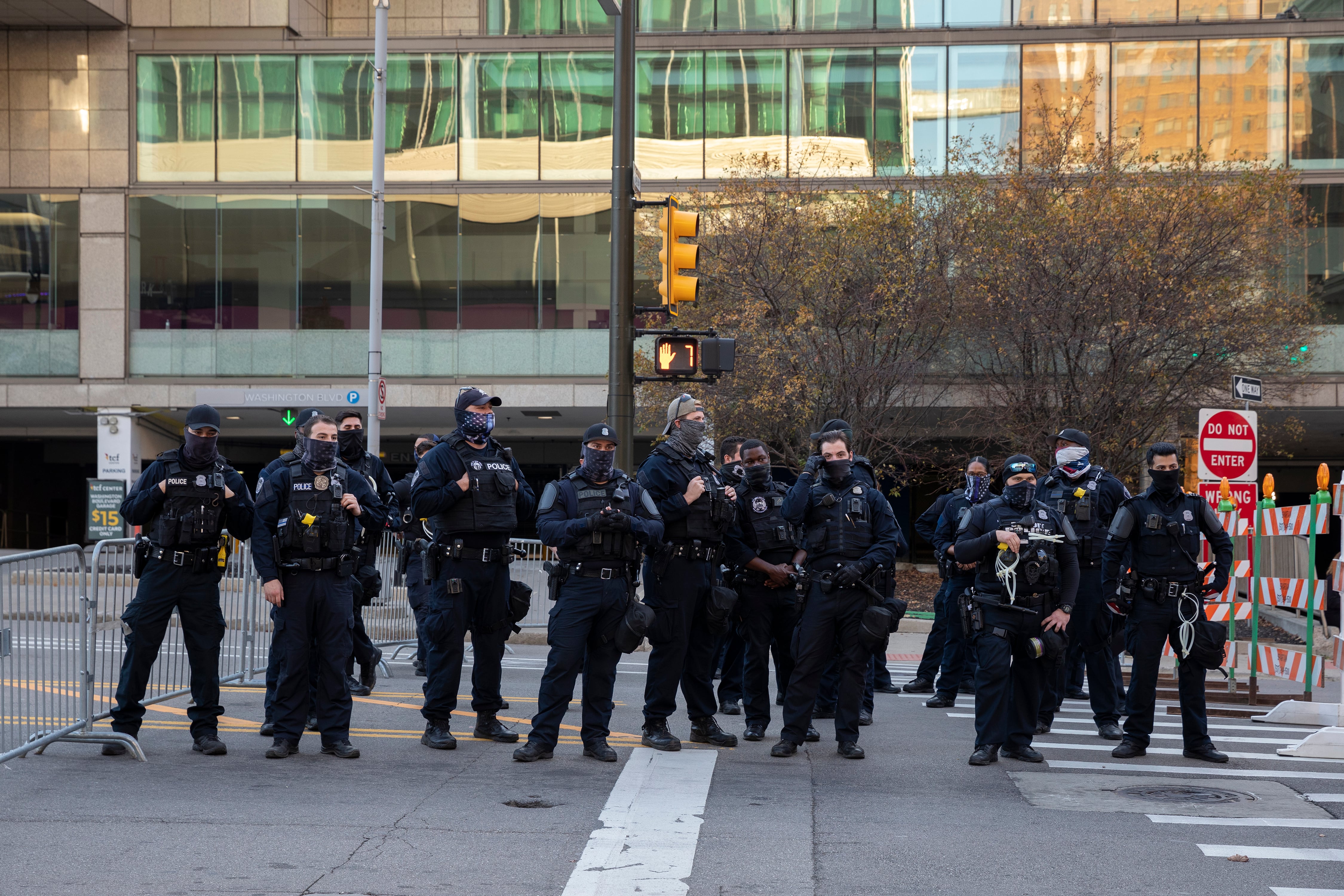 A line of police in riot gear stand in front of a large building waiting for protestors.