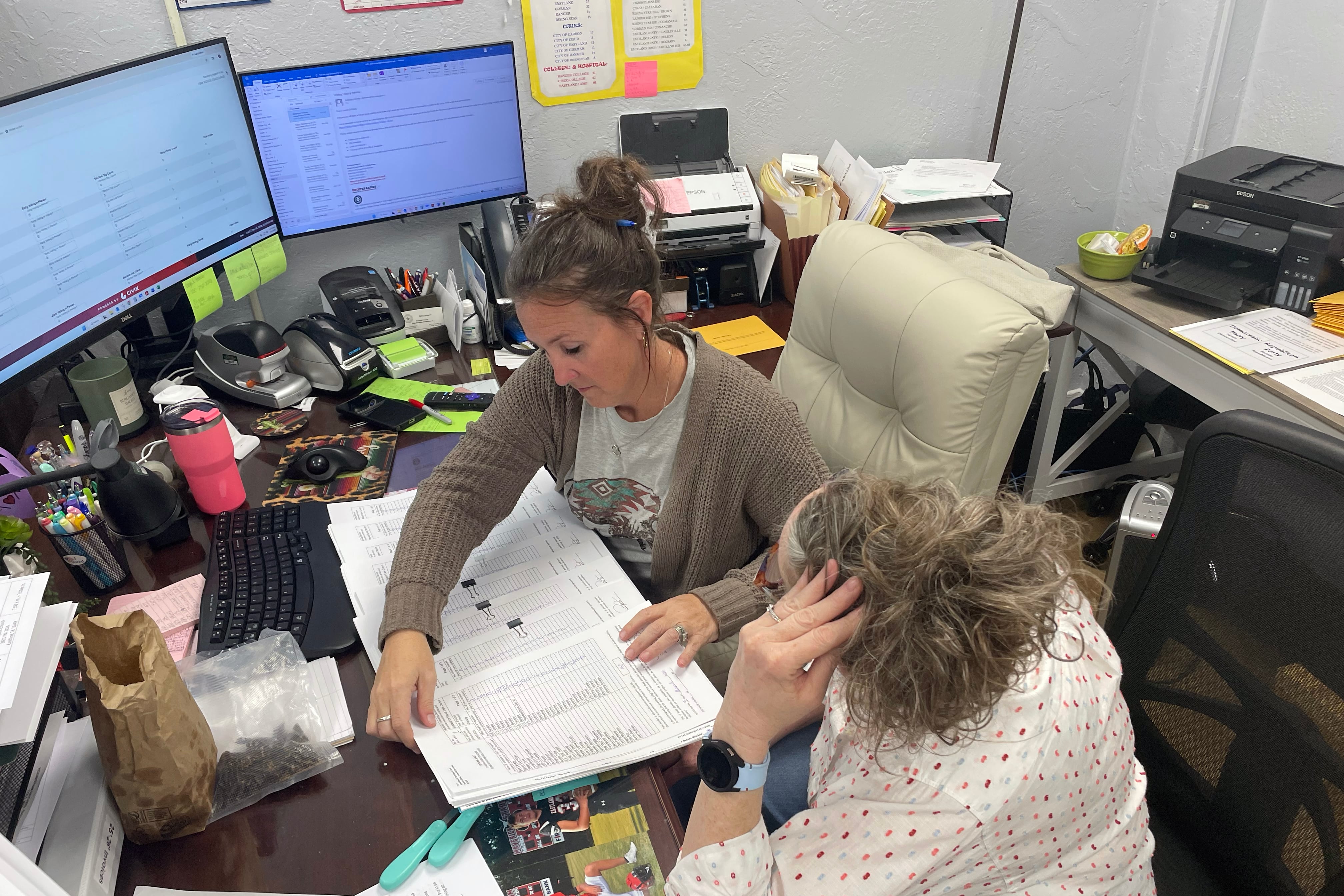 A photograph of two white women working at a desk in an office room.