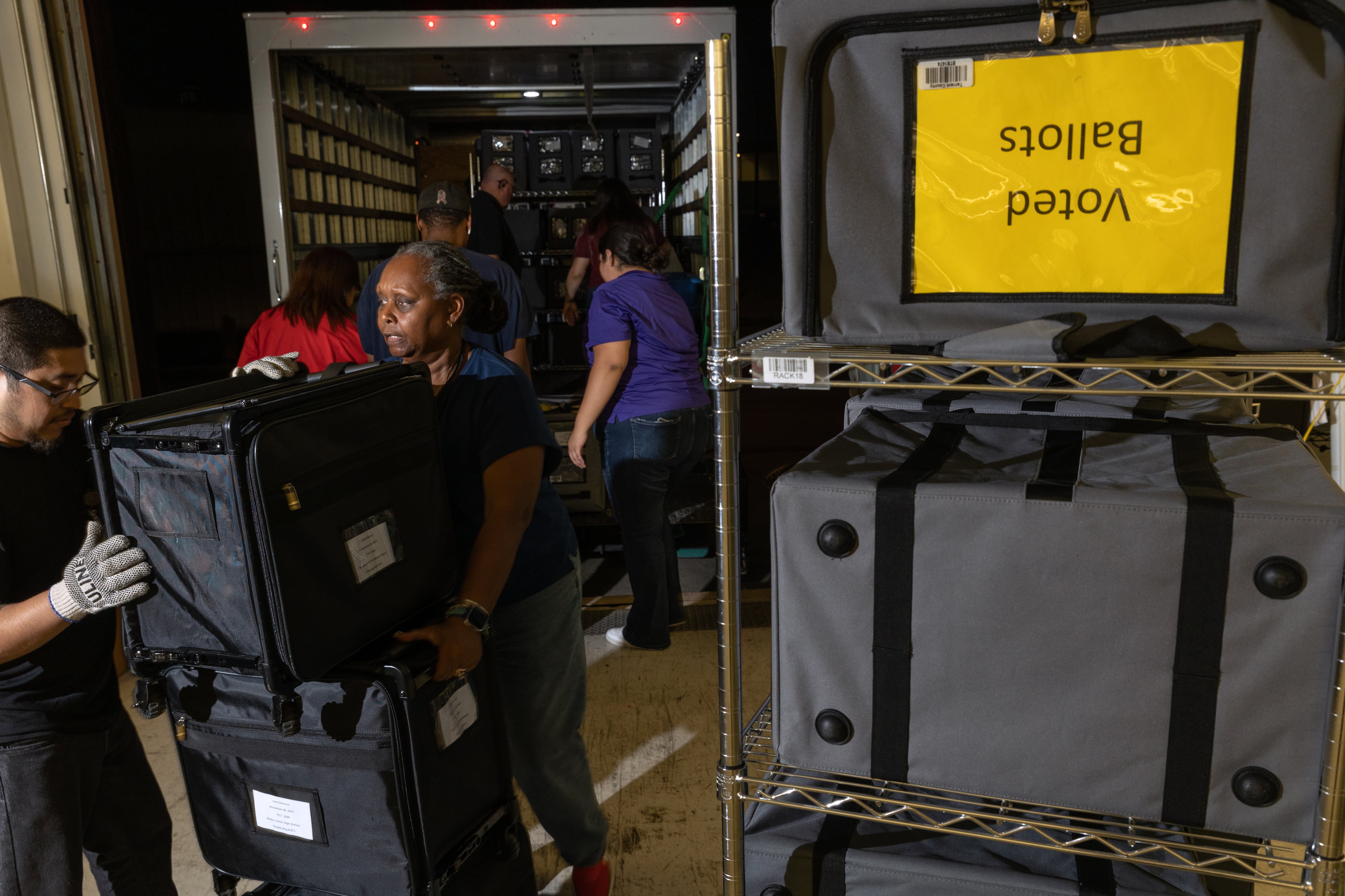 Workers unload large cases out of a truck into a building