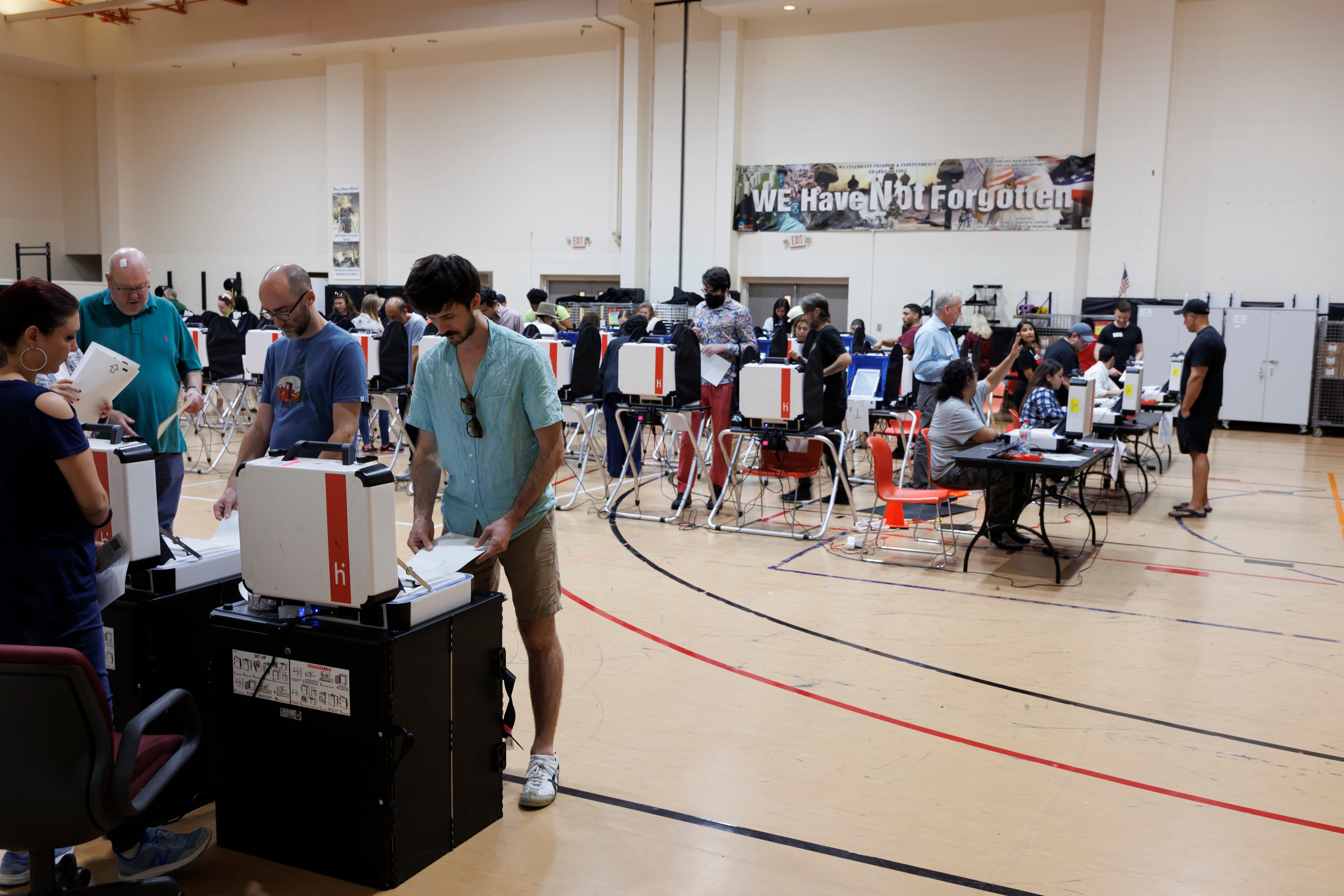 A gymnasium filled with tables of voting machines and people