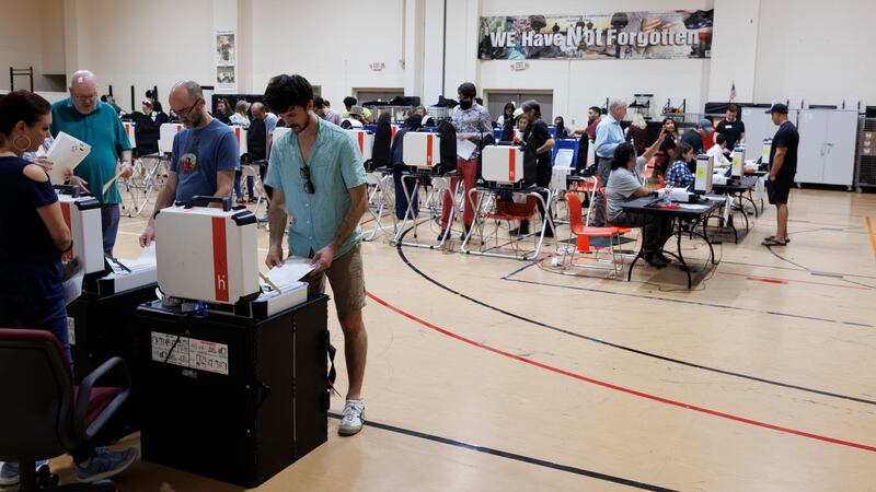 A gymnasium filled with tables of voting machines and people