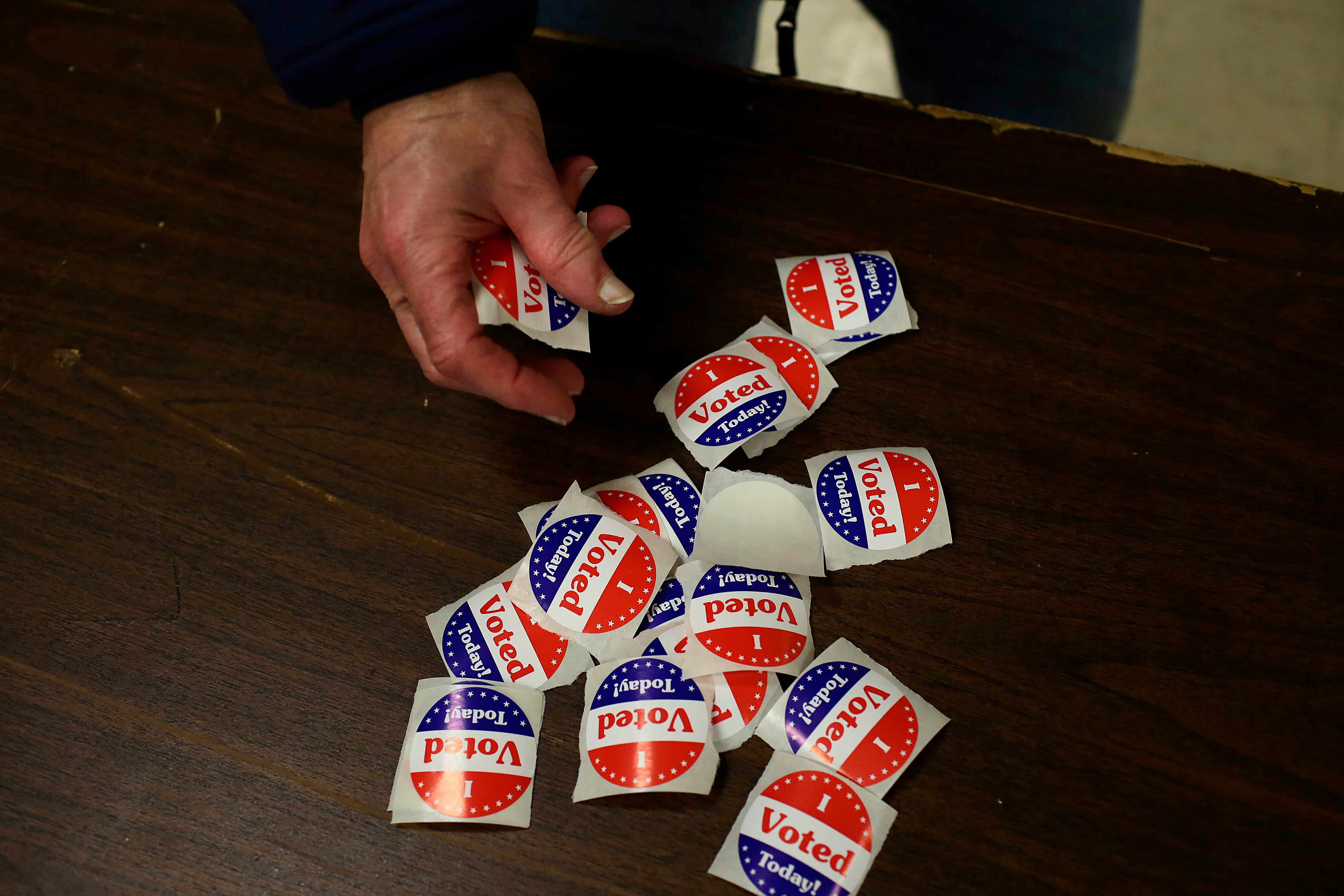 A hand reaches out to grab an "I Voted" sticker on a table.