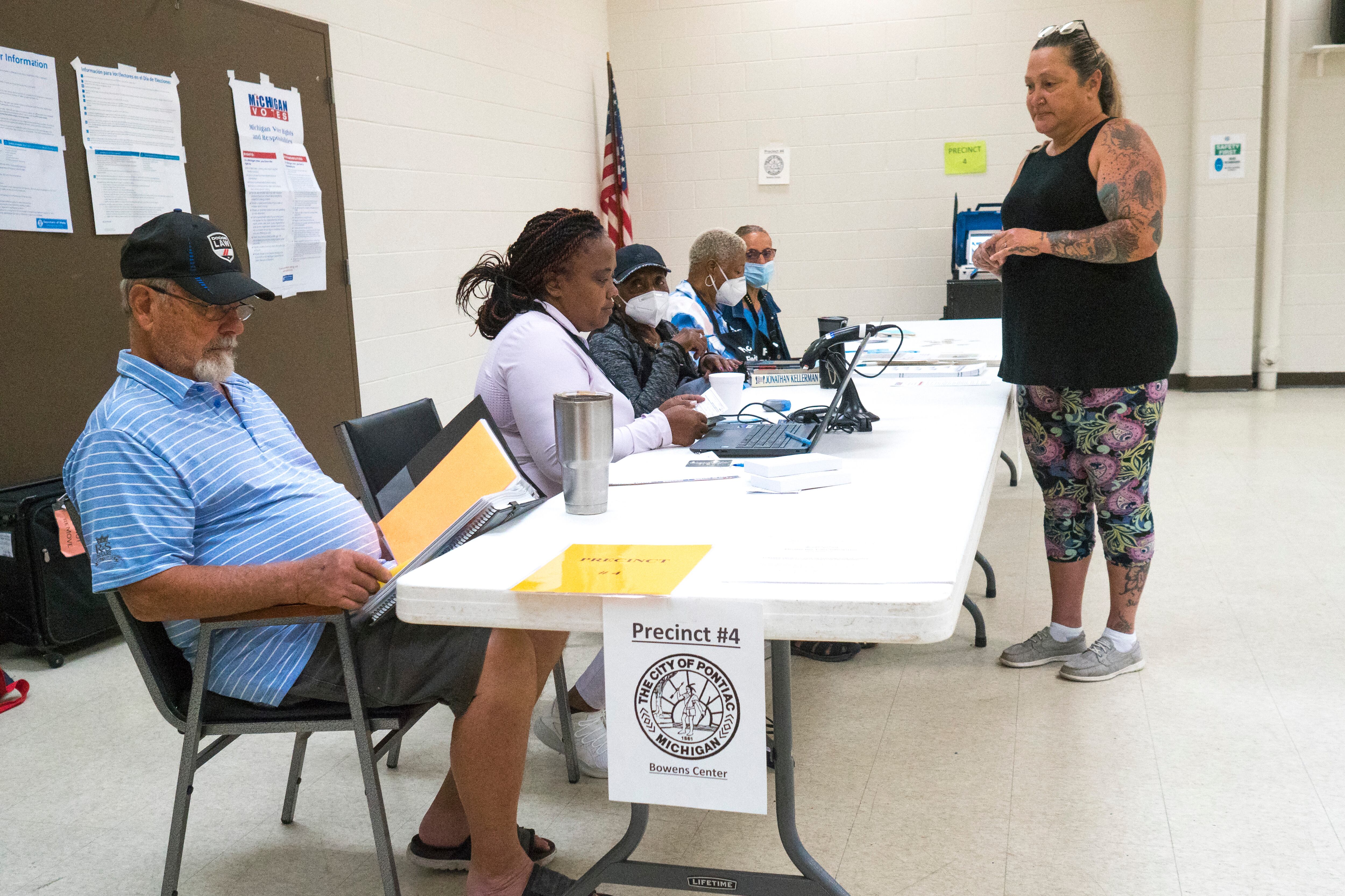 Workers seated at a table in a community room check computers while a voter waits