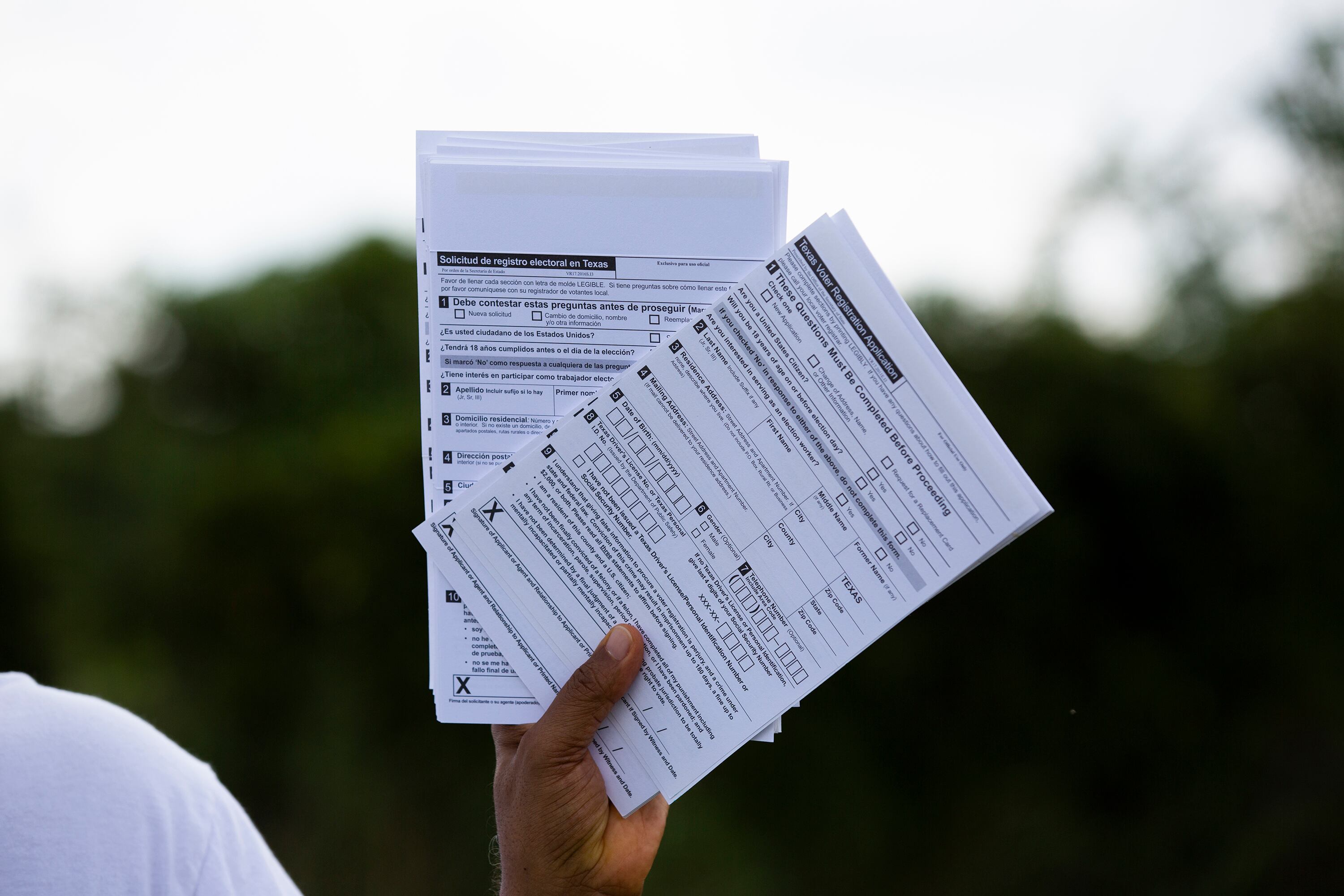A hand holds up two stacks of while paper with black writing on it with a dark green background outside.
