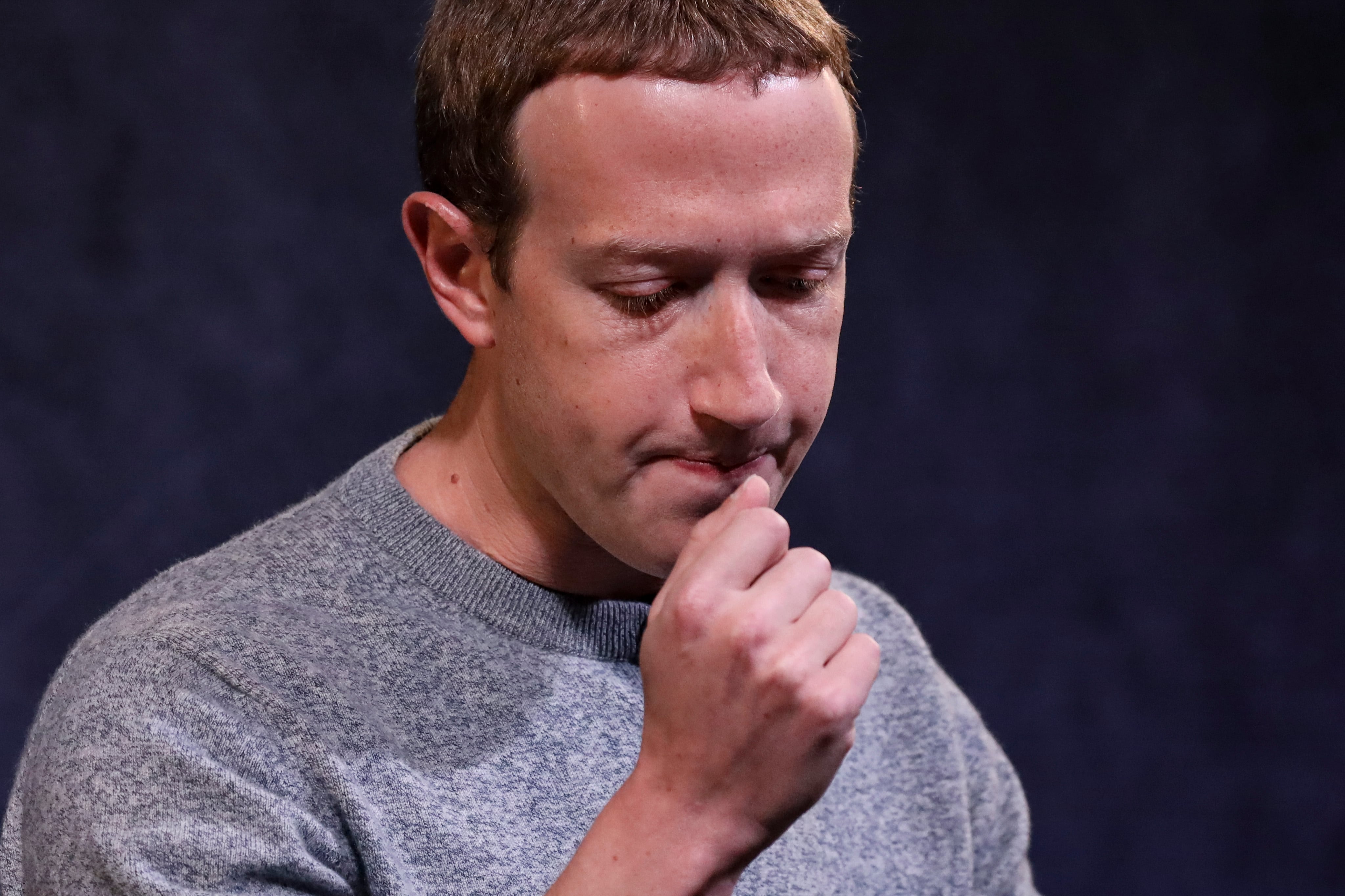 A closeup of Mark Zuckerberg gazing down with finger held to chin as if lost in thought