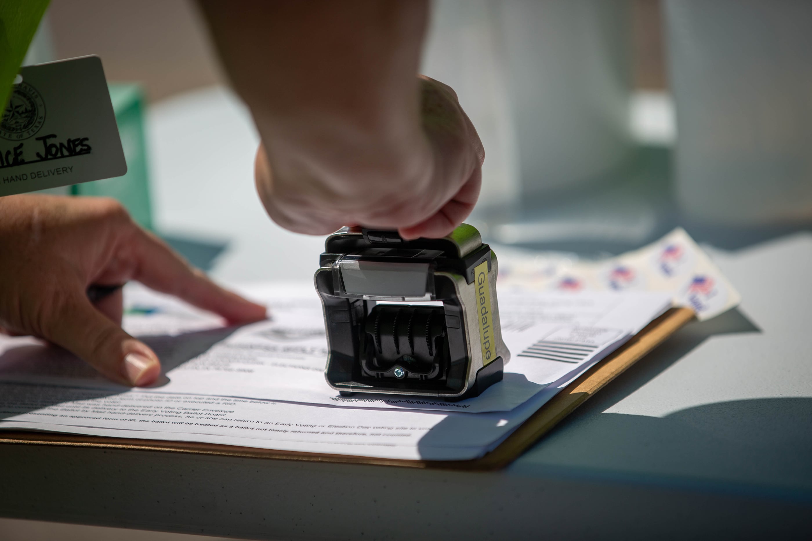 A close up of a hand using a stamp to mark a ballot on a table.