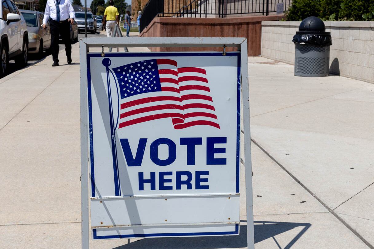 A "vote here" sign stands outside of a building on a sunny election day.