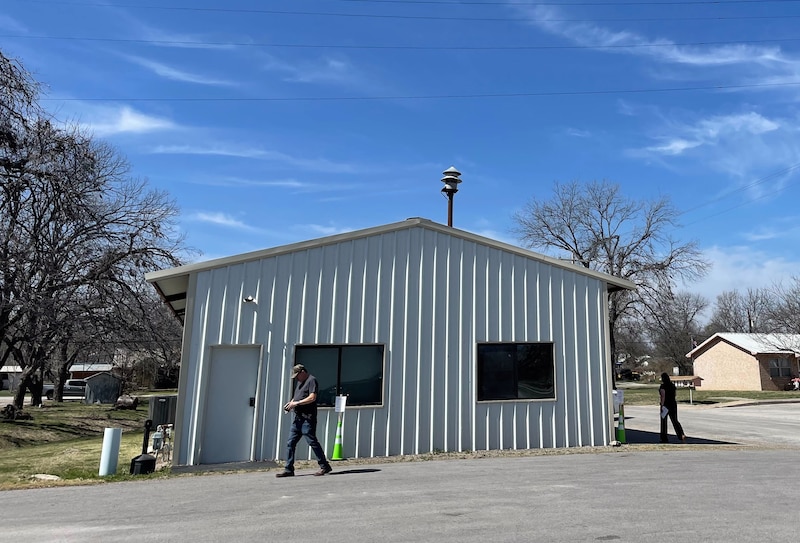 A photograph of two people standing outside of a fire house on a sunny day.