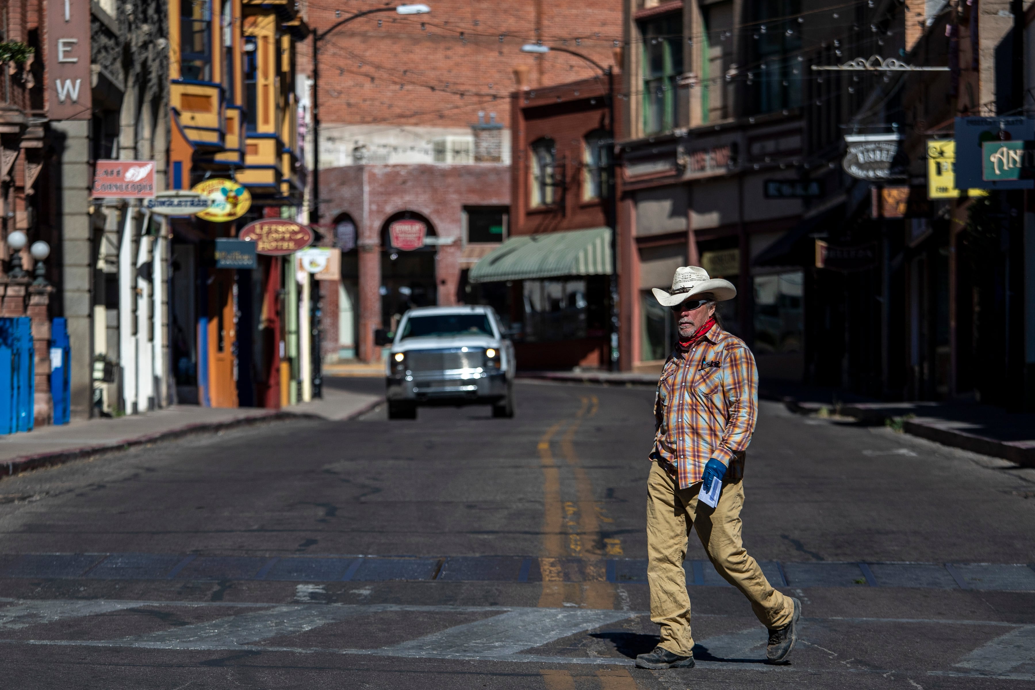 A man in a cowboy hat crosses a street lined by old buildings