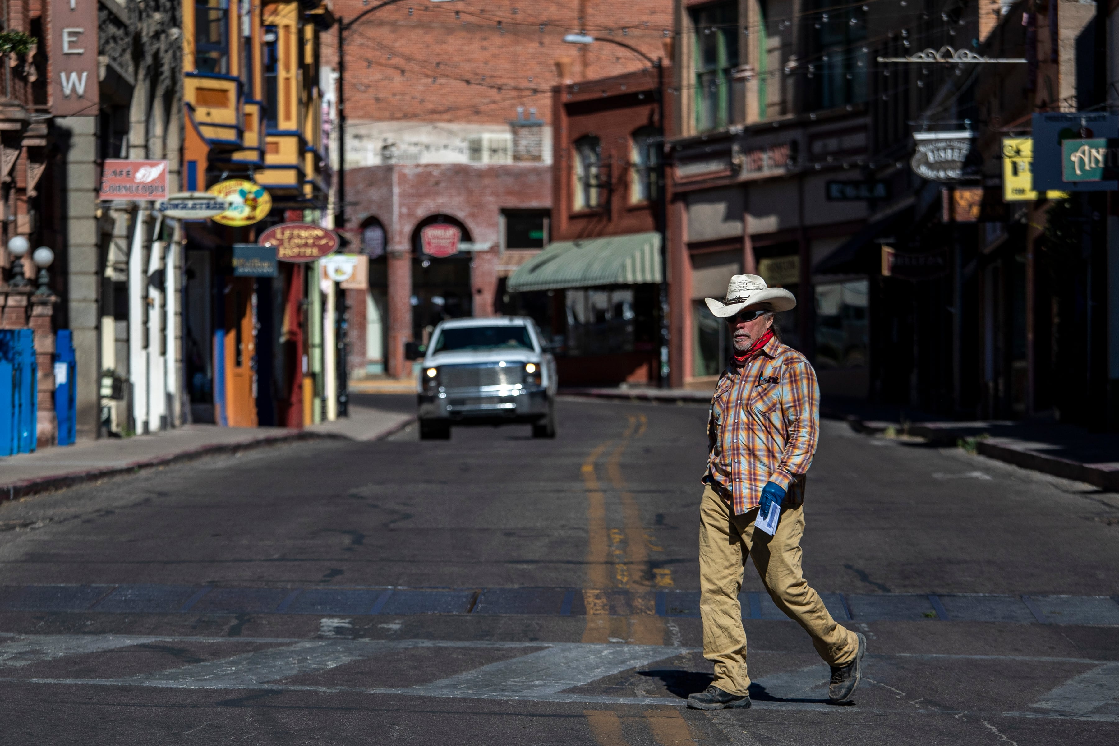 A man in a cowboy hat crosses a street lined by old buildings