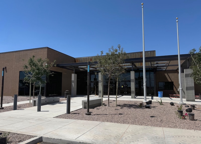 The outside of large brick building with two flag poles and some trees out front.