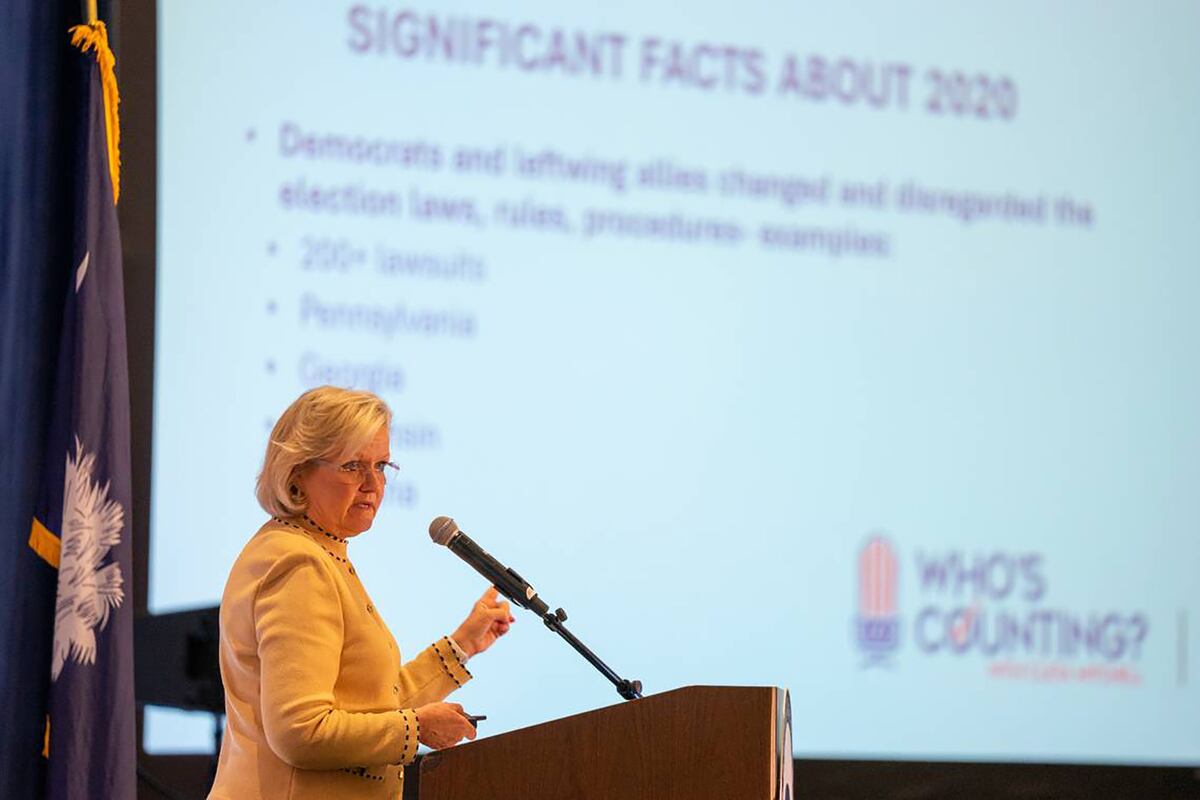 A woman stands at a podium with a microphone before a large screen with a slide that starts “Significant facts about 2020”