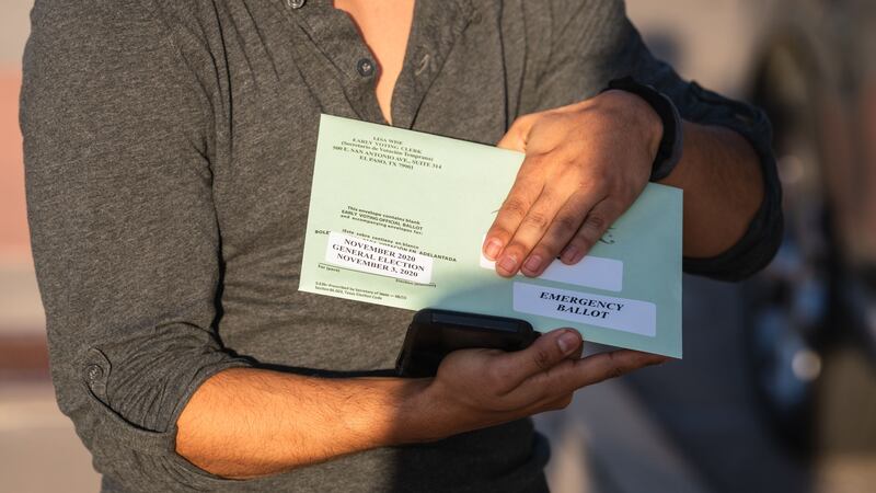 A person holds a green ballot envelope that reads “November 2020 election” and “emergency ballot.”