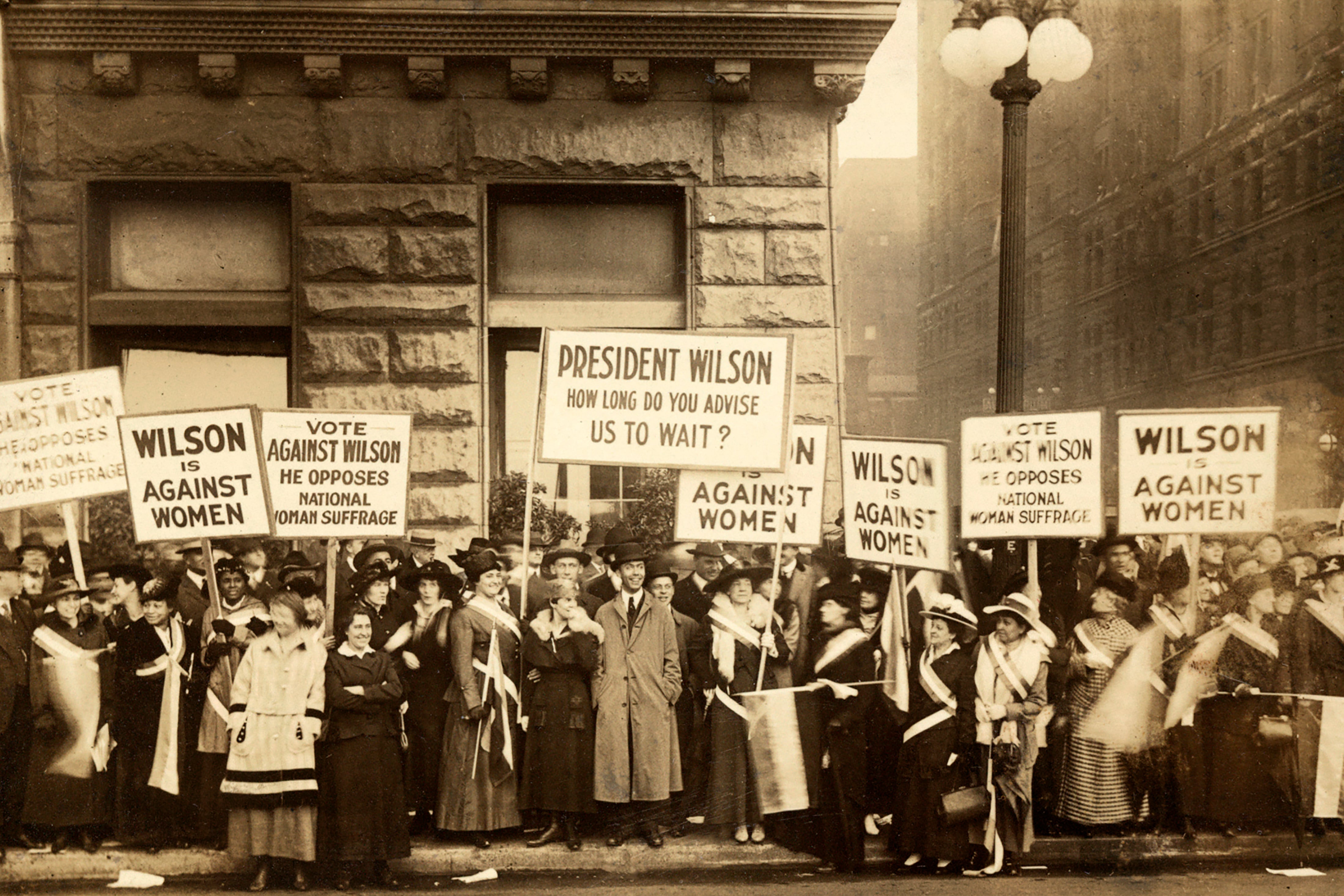 A sepia tone image of women standing on a street corner holding signs.