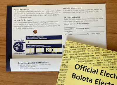 A white and blue mail in voting ballot on a wood table.