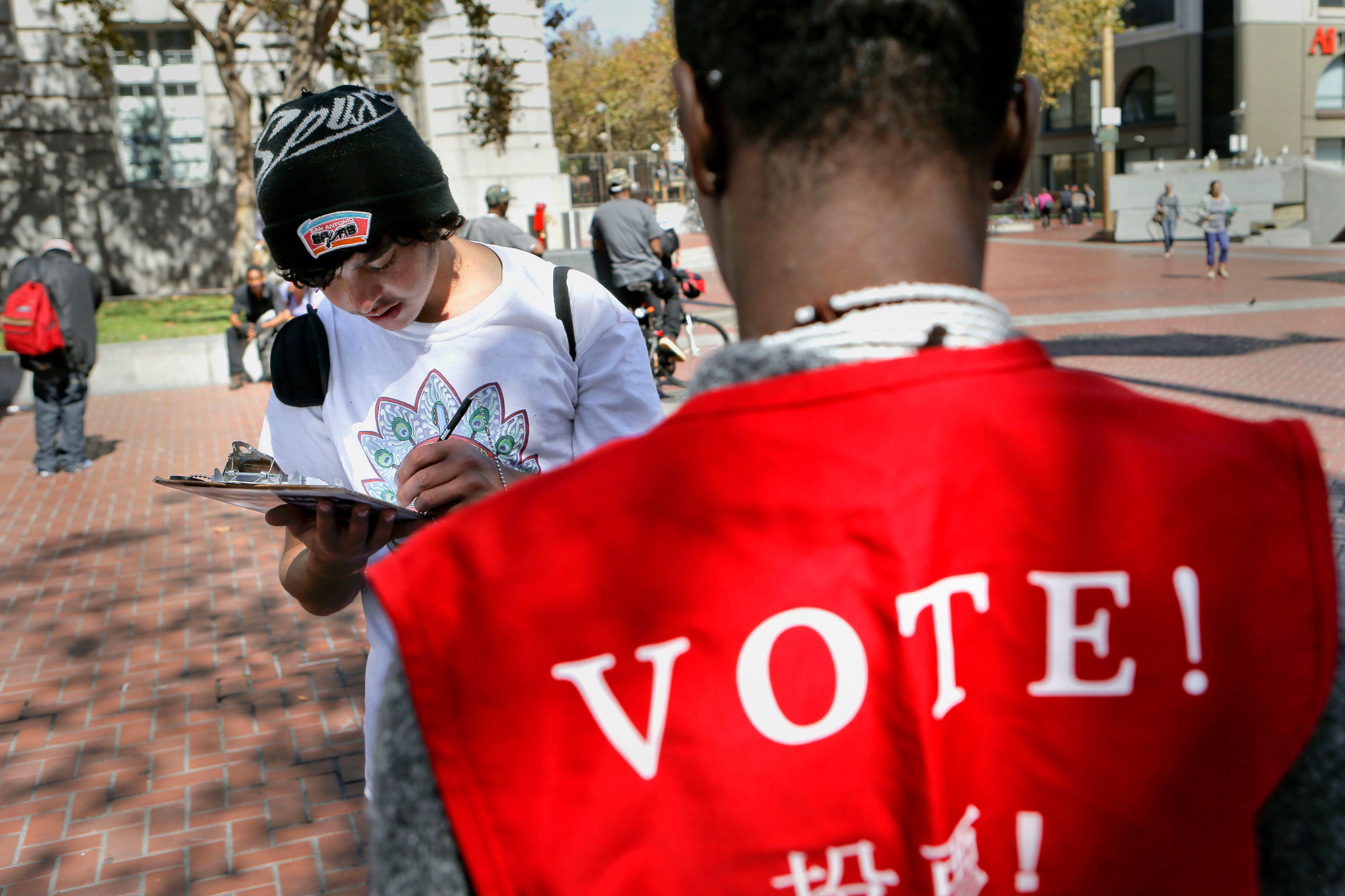 Man in red vest stands in front of someone filling out a form.