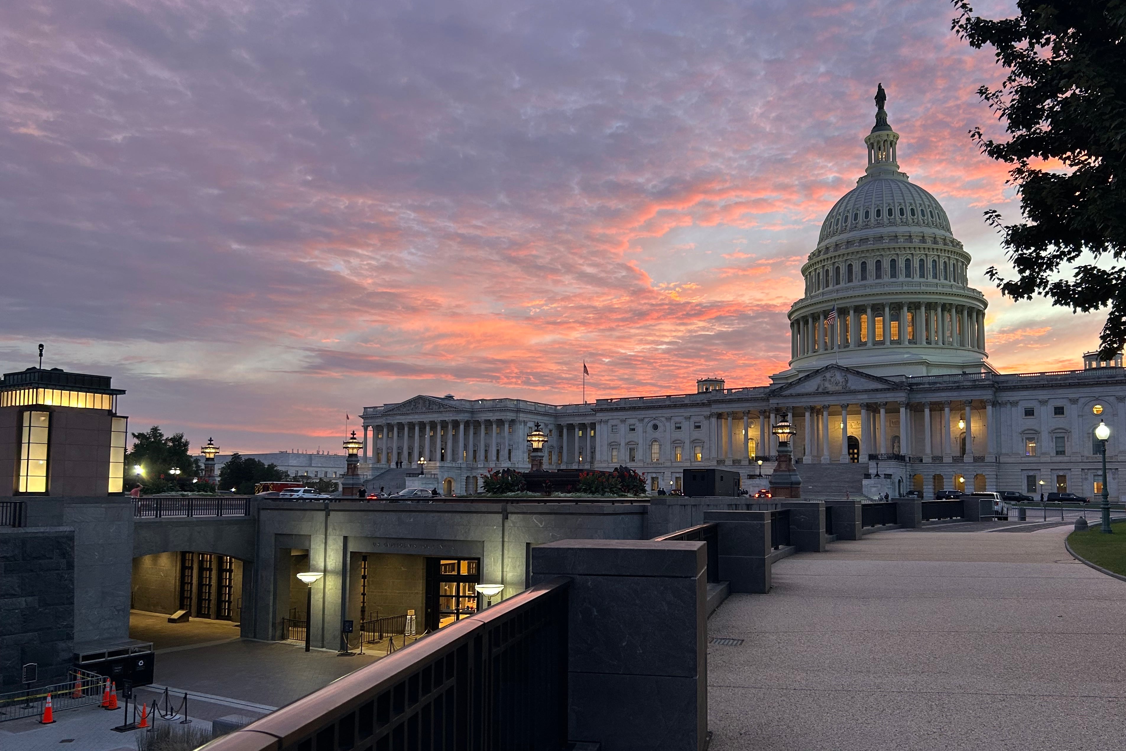A photograph of the U.S. Capitol building with a vibrant sunset showing pink, purple and orange colors in the sky.