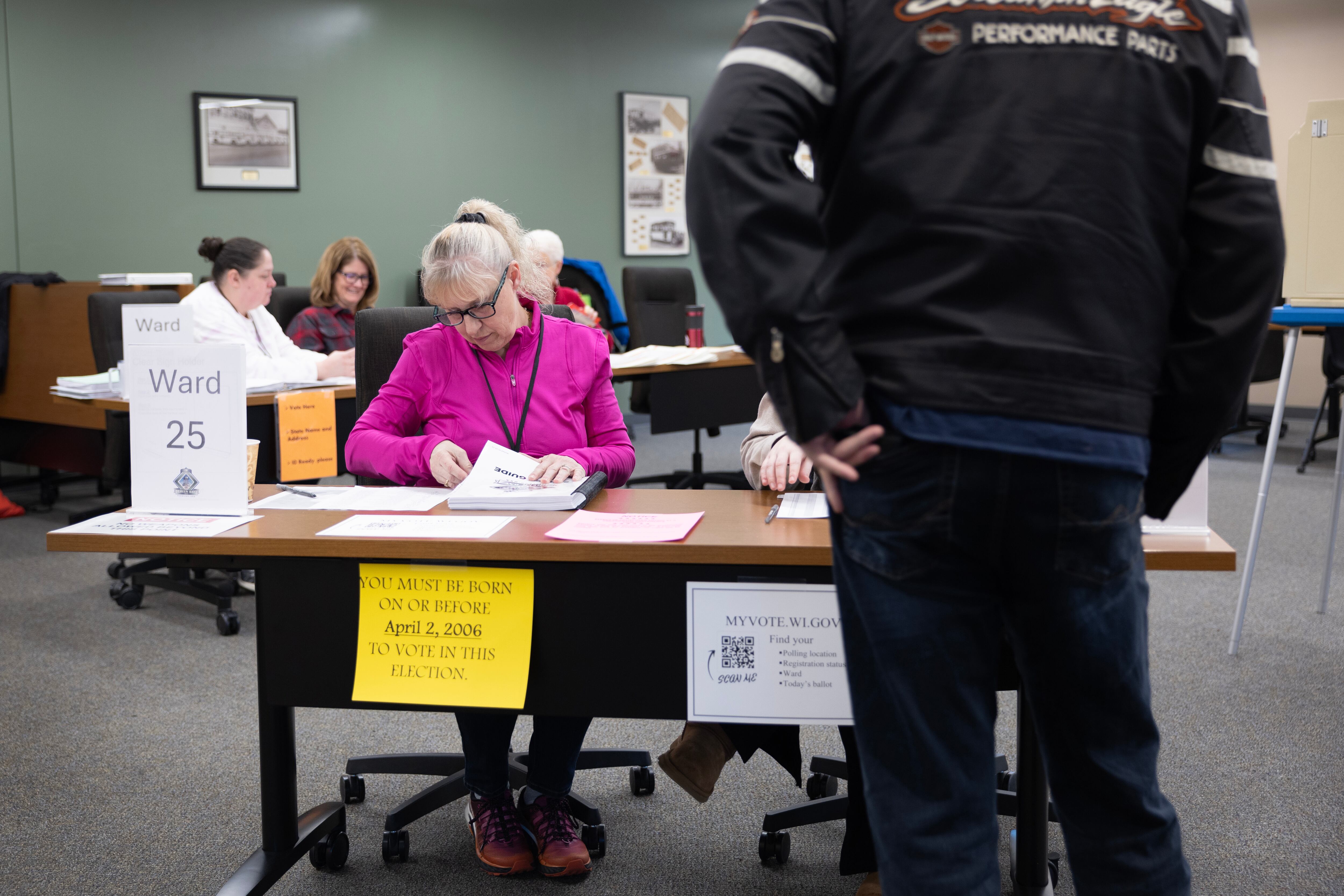 A person sits down at a table in a room while a person is standing in front of the table.