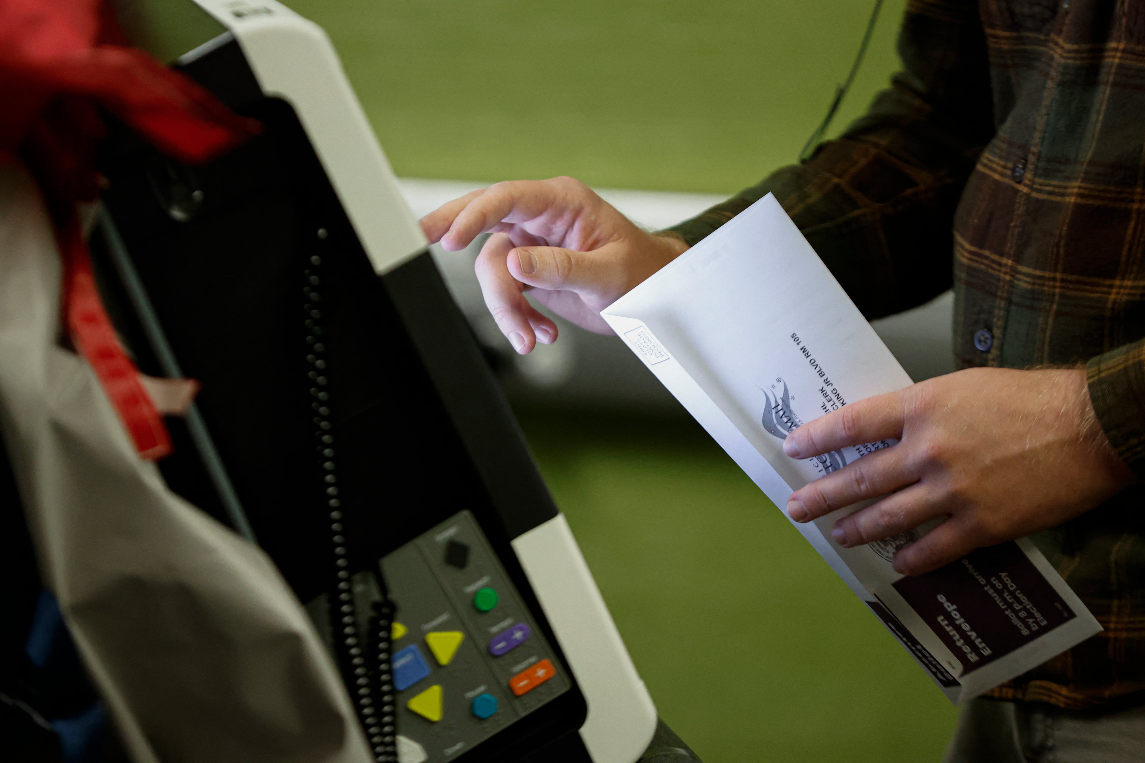 A person holds a ballot and reaches out to type on a screen.