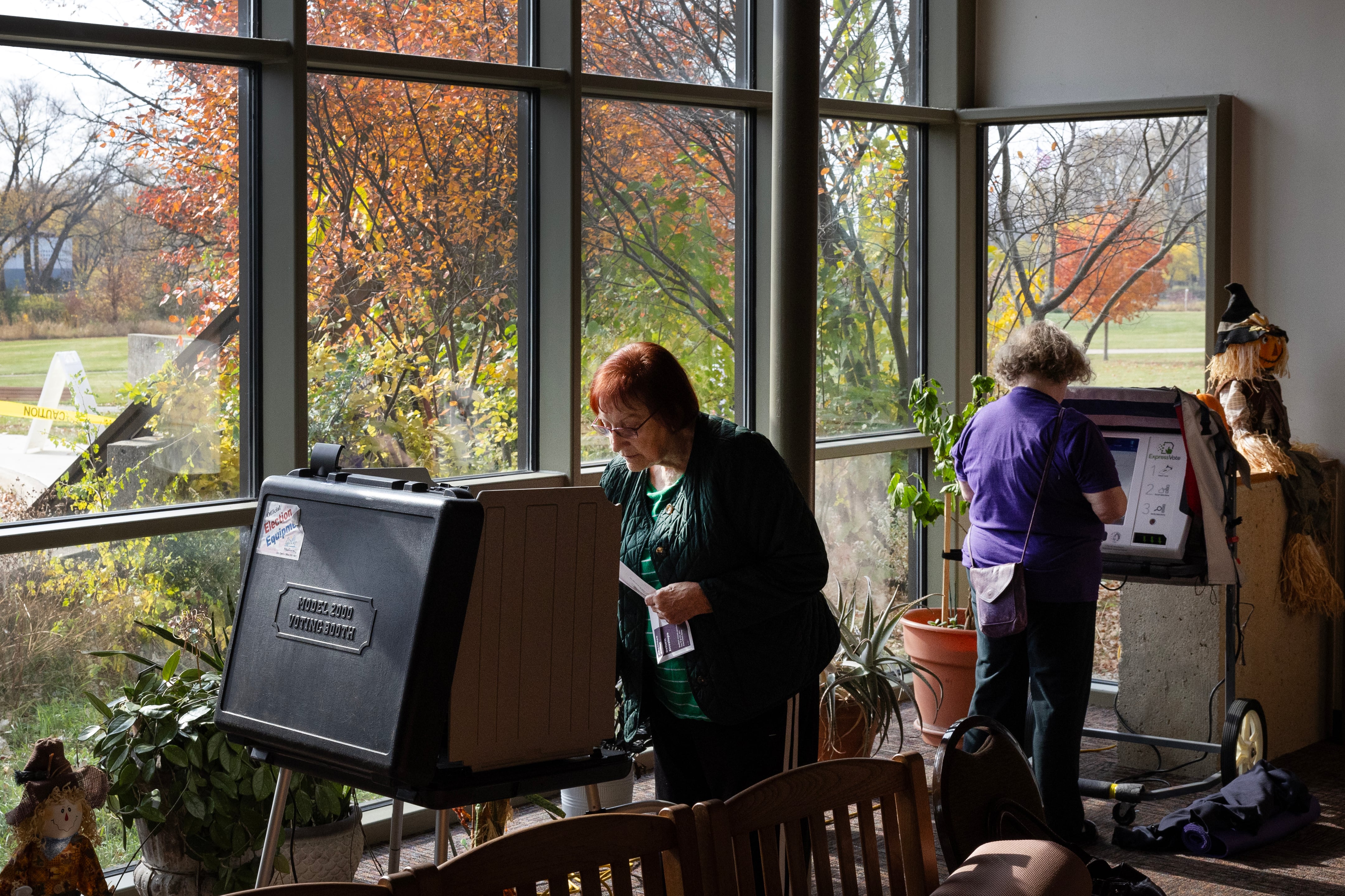 Two people stand back to back filling out their ballots in a room with one wall in the background made of all windows.
