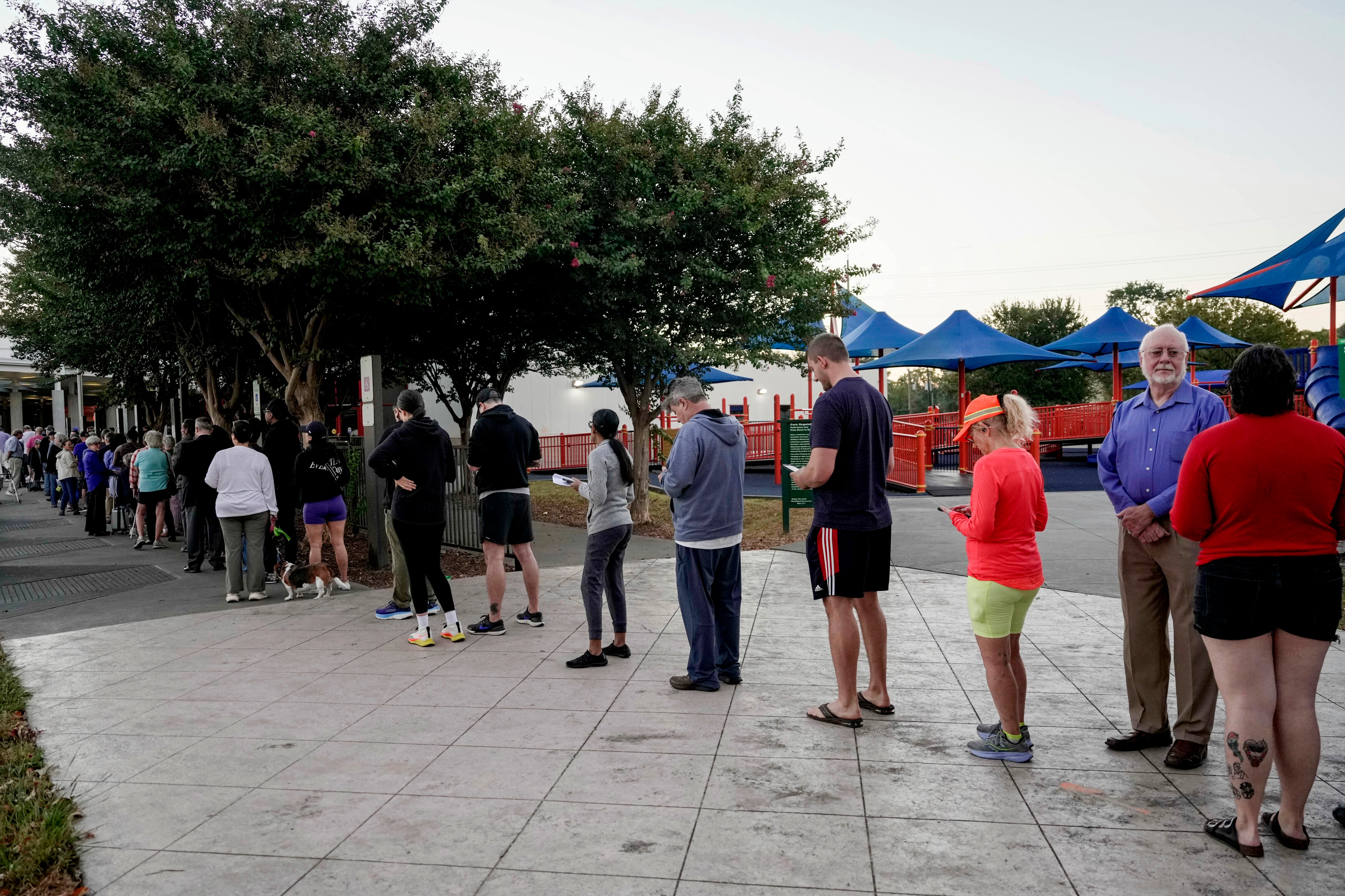 A long line of people stand outside of a building and wait to vote.